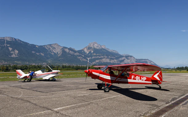 Two small airplanes parked on tarmac with mountains behind.