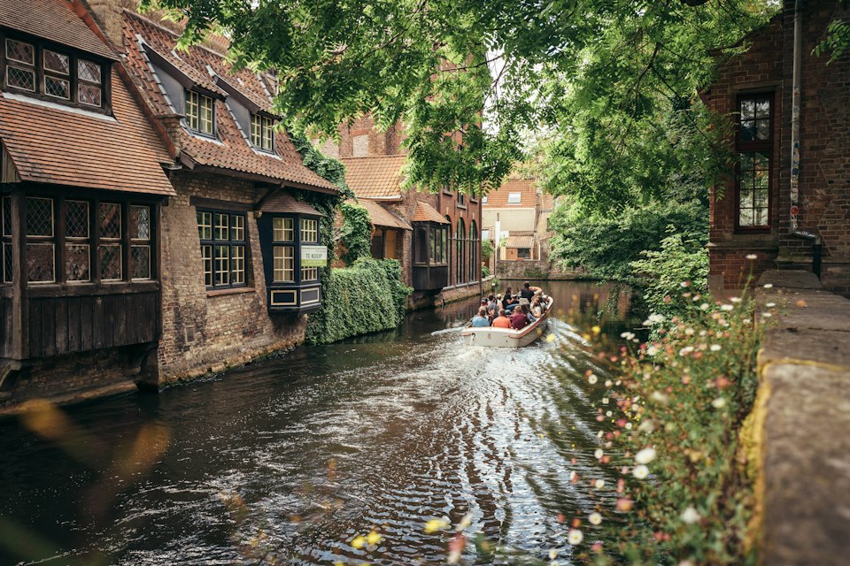 A tour boat navigating a narrow Bruges canal lined with old buildings