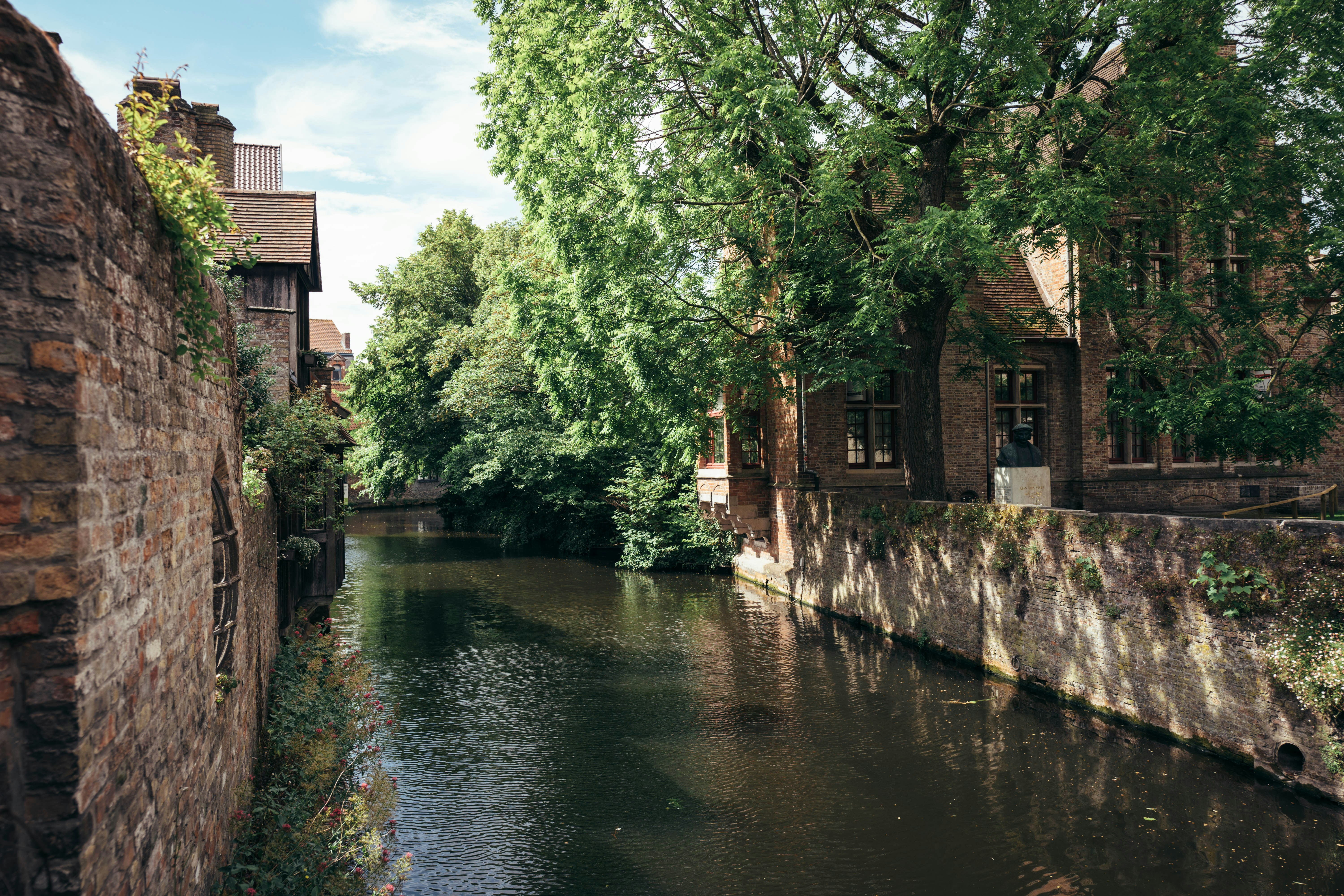 Canal with brick buildings and lush green trees.