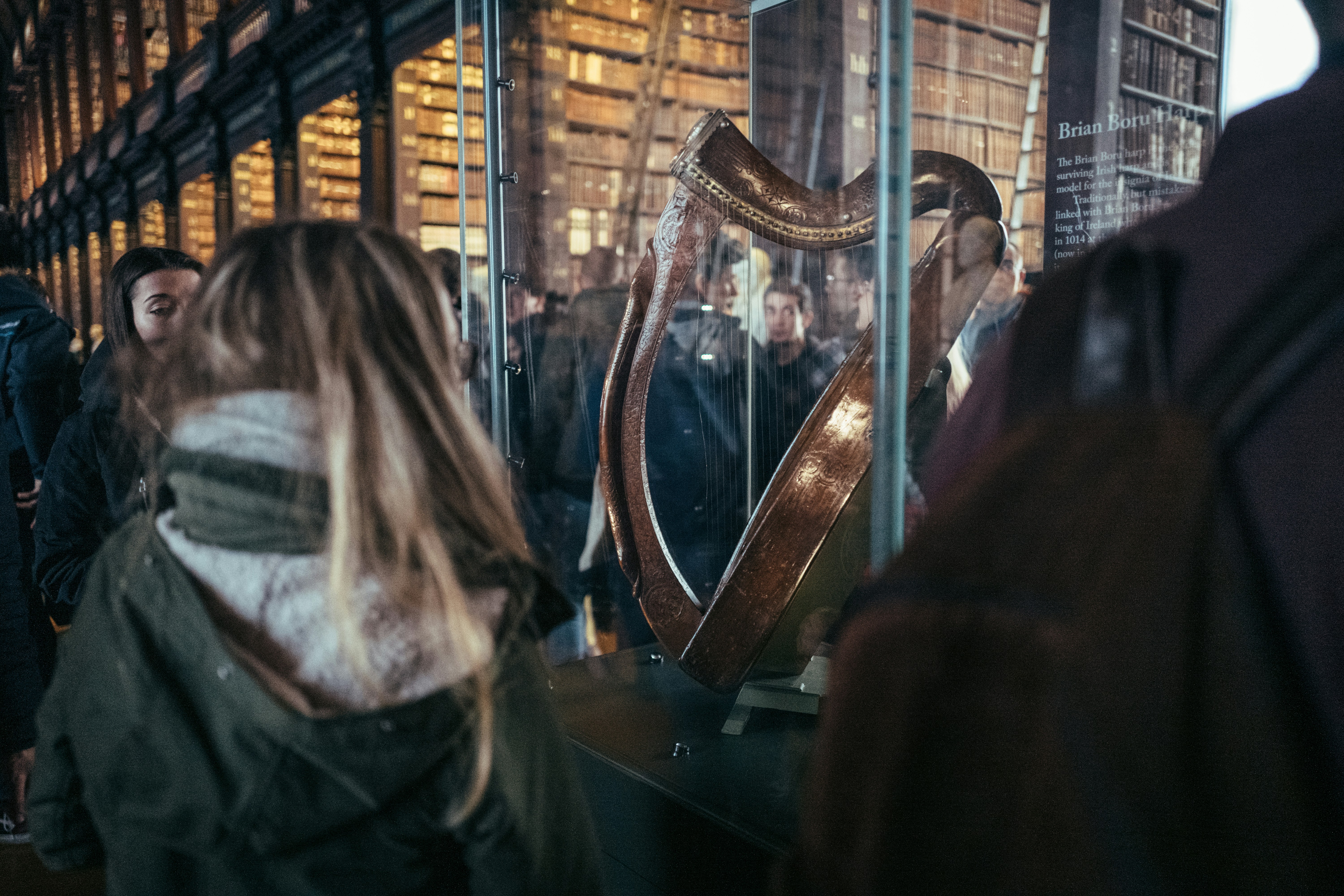 People viewing an ornate harp in a library exhibit.