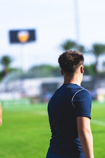 Young man on a soccer field with stadium in background.