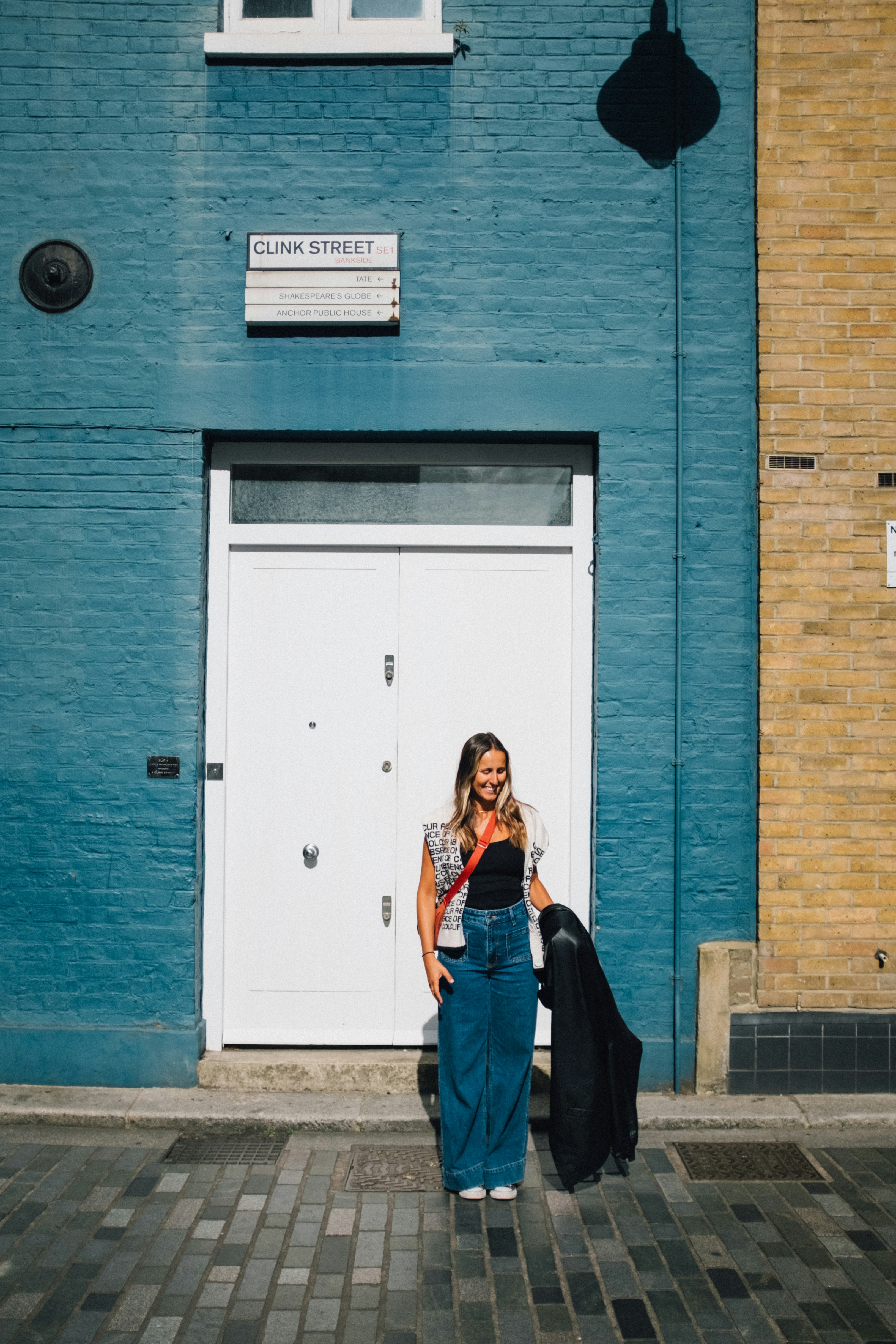 Woman standing outside blue brick building with white door