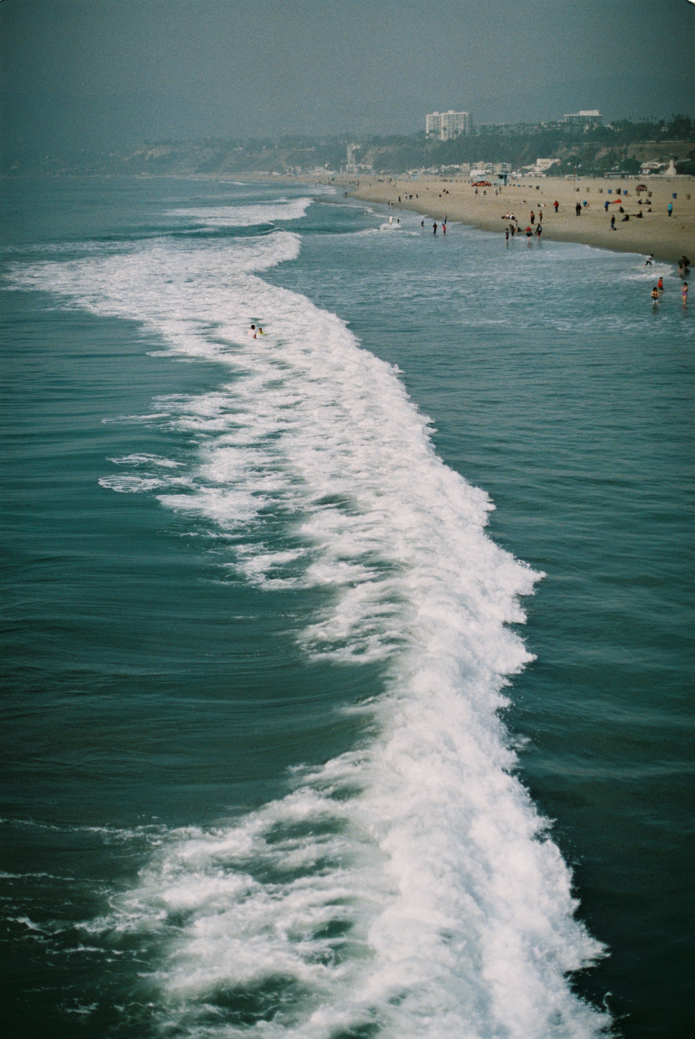 Wellen brechen an einem Strand, Menschen gehen zu Fuß.