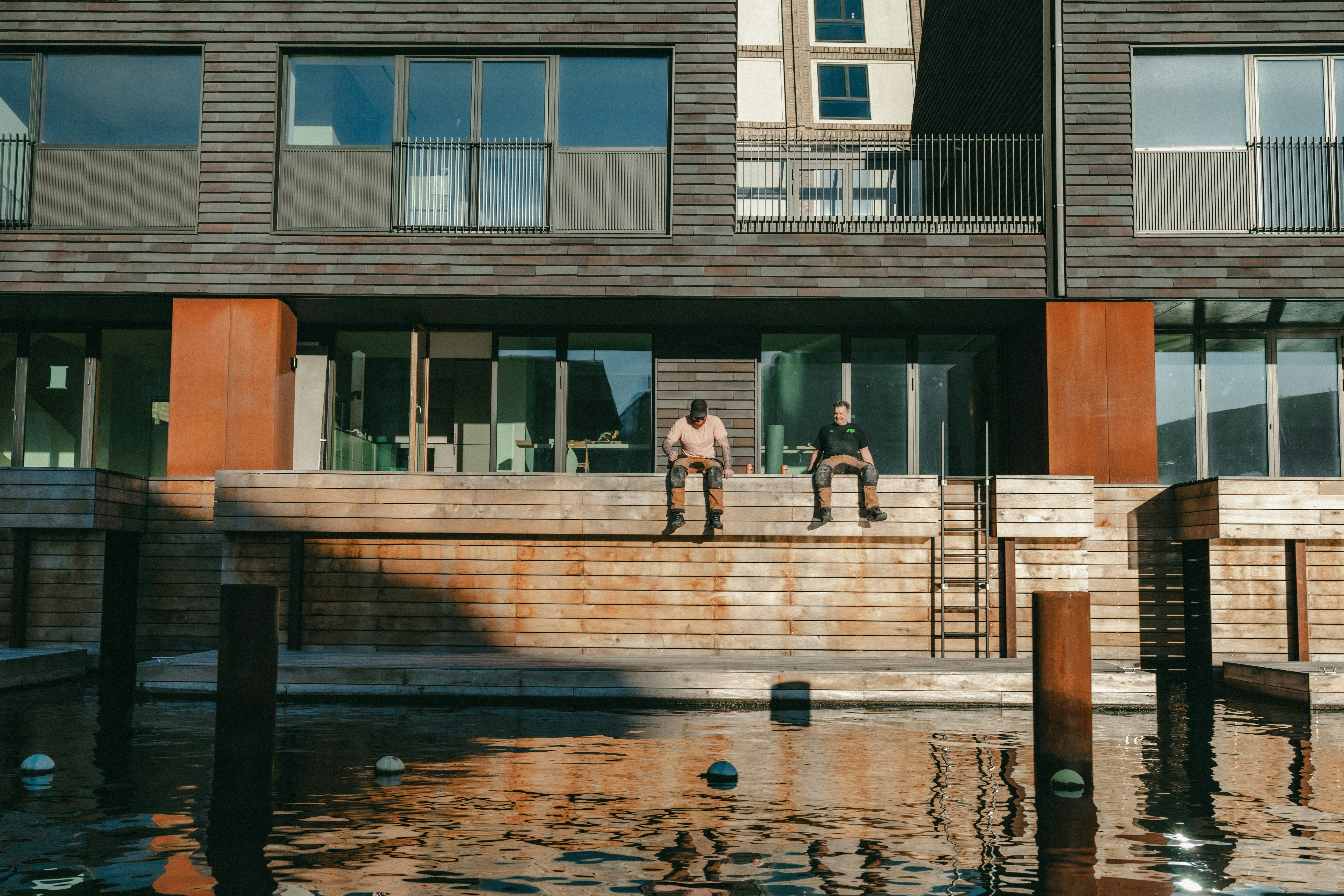 Two men sitting on a ledge by the water.