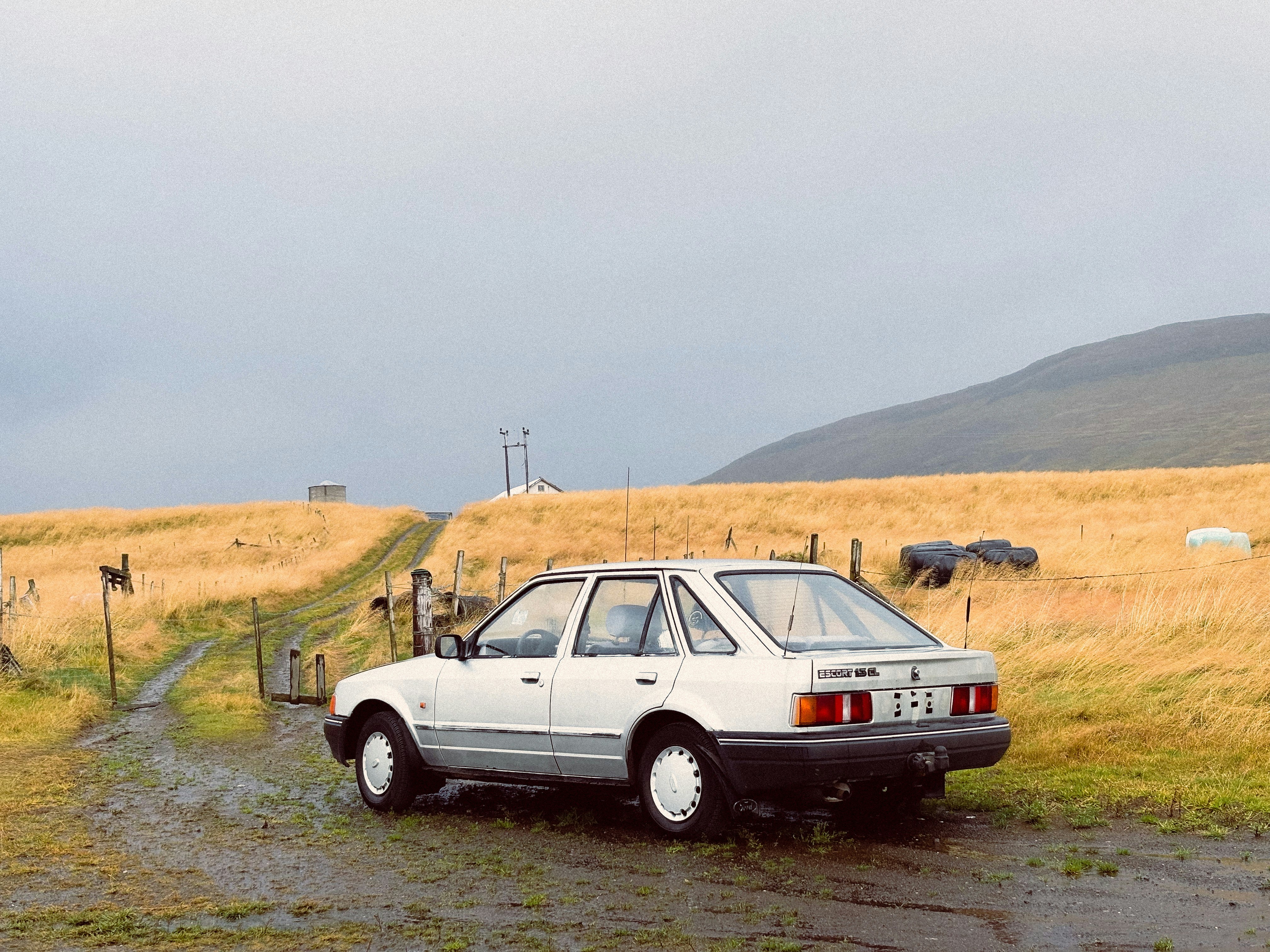 White hatchback parked on a muddy rural road.