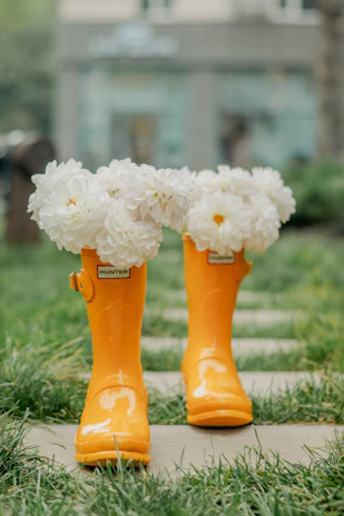 Orange rain boots filled with white flowers outdoors.