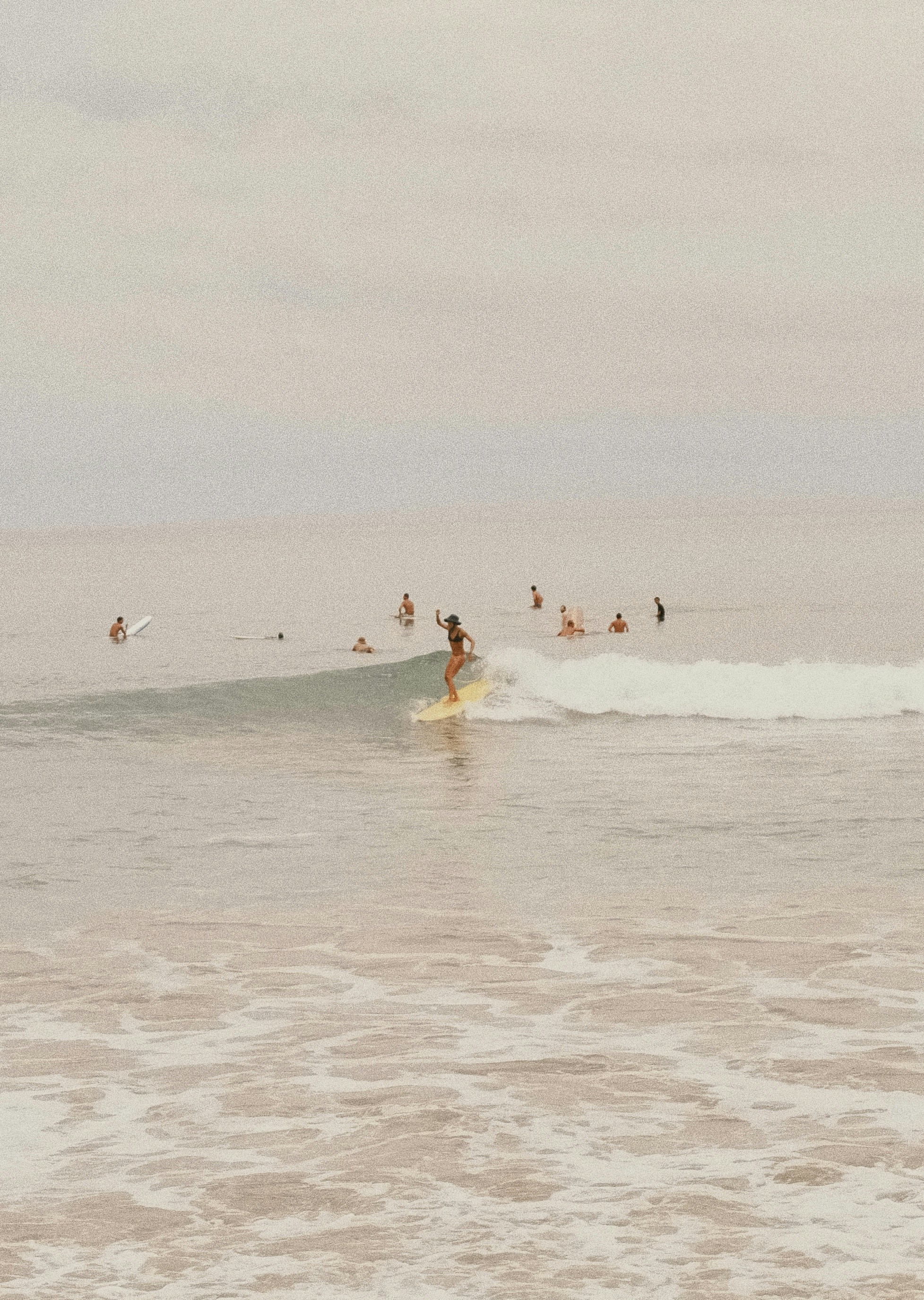 Surfer rides a wave with others in the ocean.