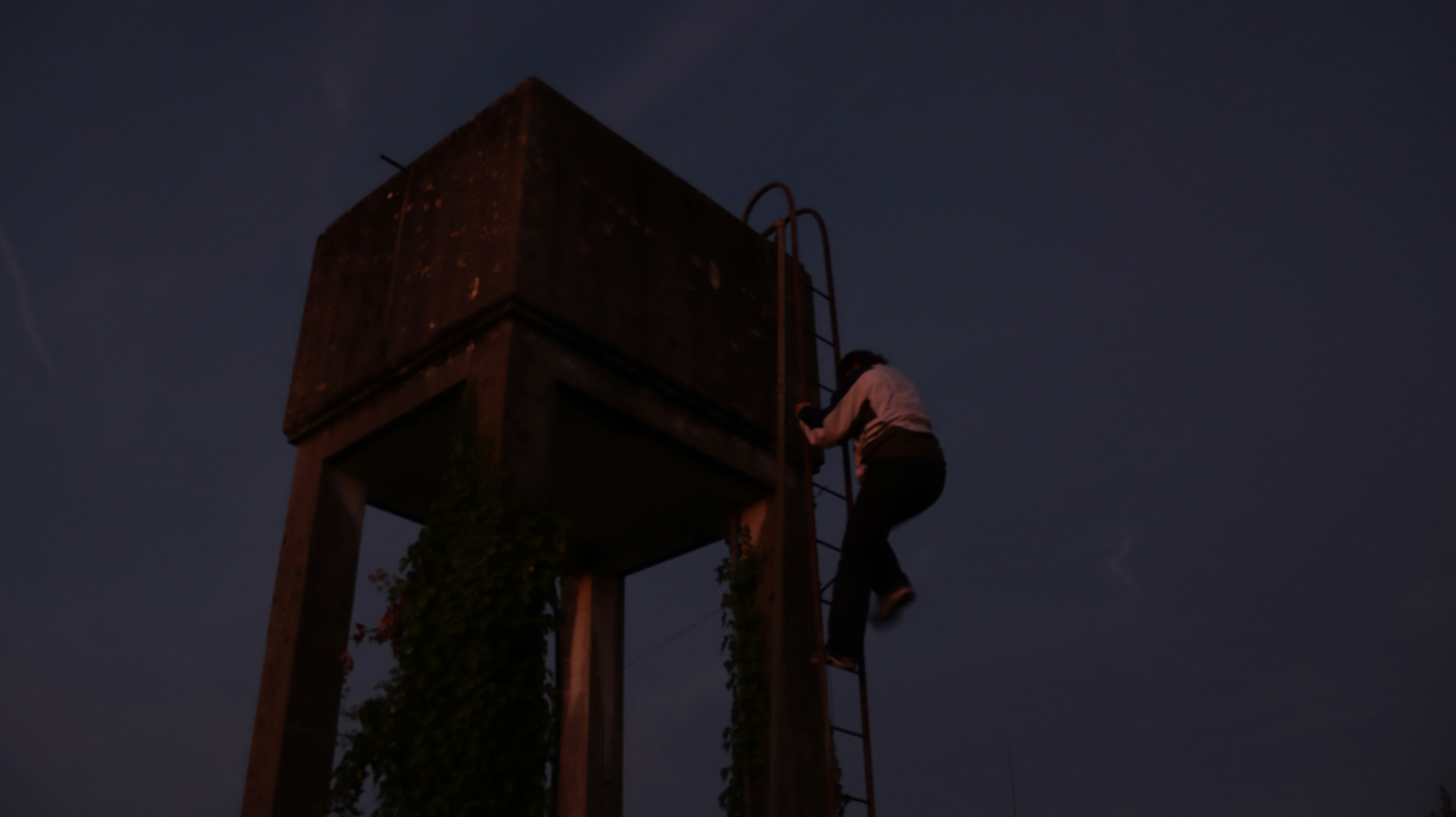 Person climbing a tall water tower at dusk