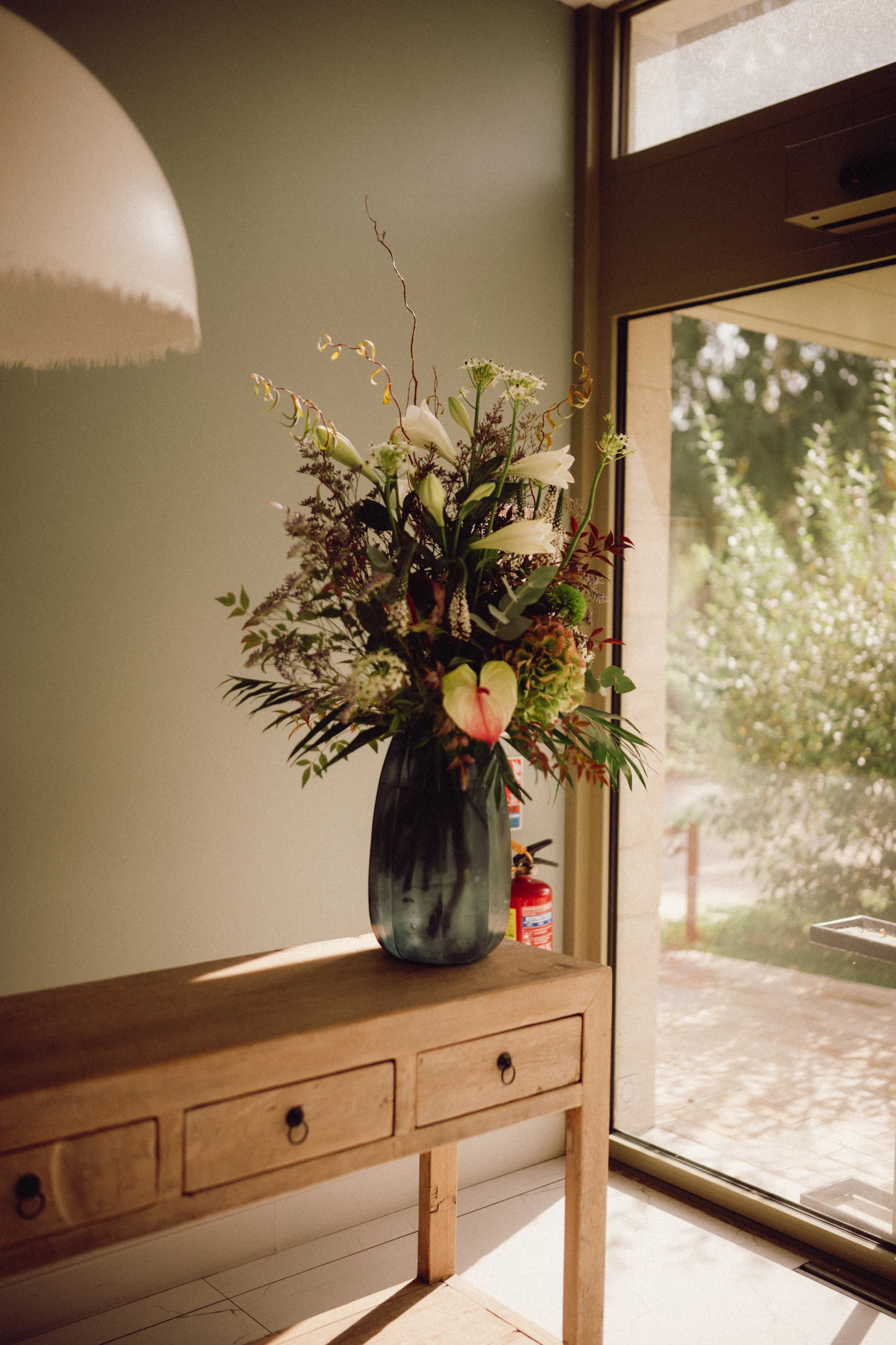 Lush silk floral arrangement styled on a wooden console table in a sunlit entryway