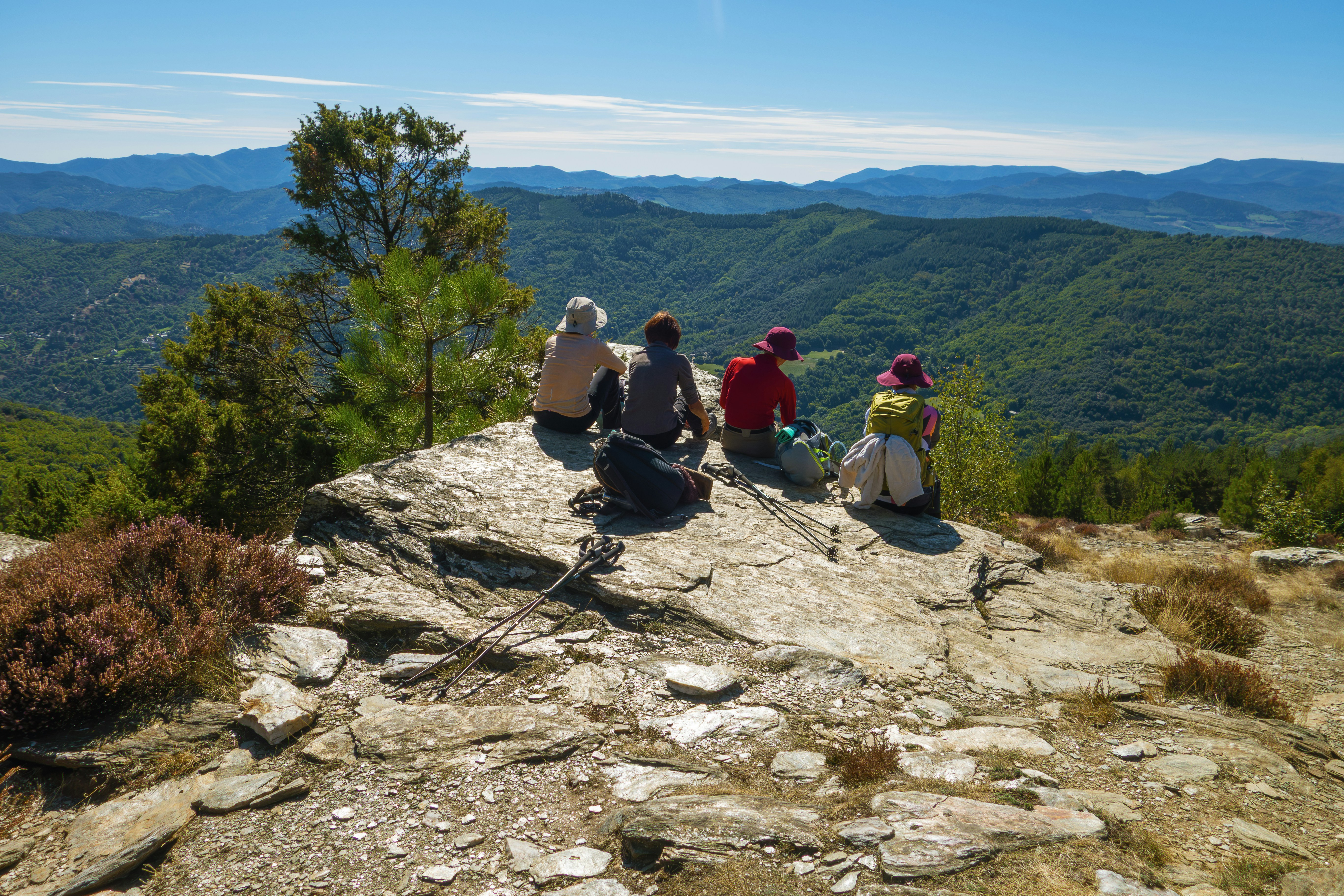 Four hikers resting on a rocky mountain summit overlooking hills.