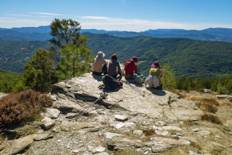 Four hikers resting on a rocky mountain summit overlooking hills.