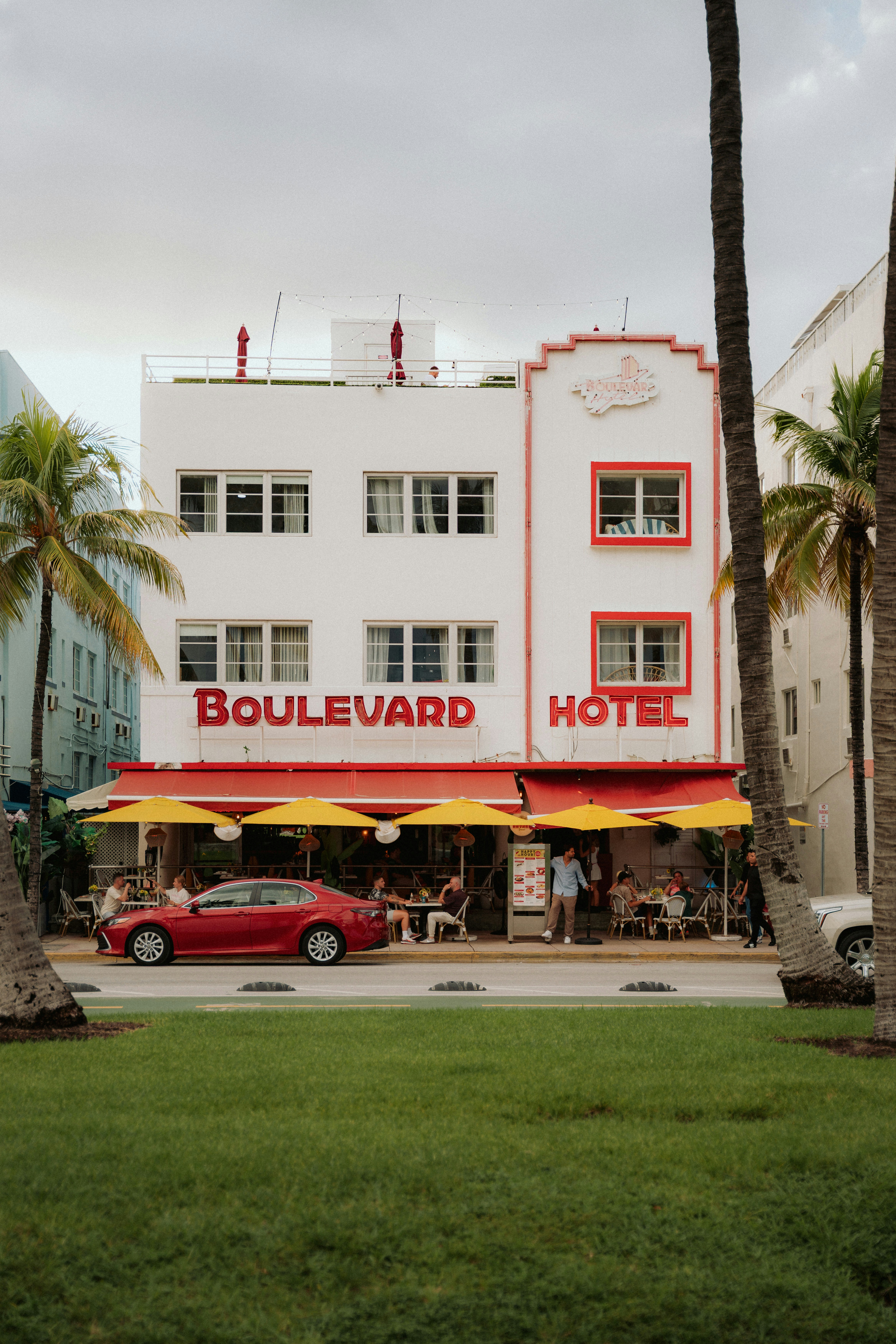 Boulevard hotel with outdoor seating and red car.