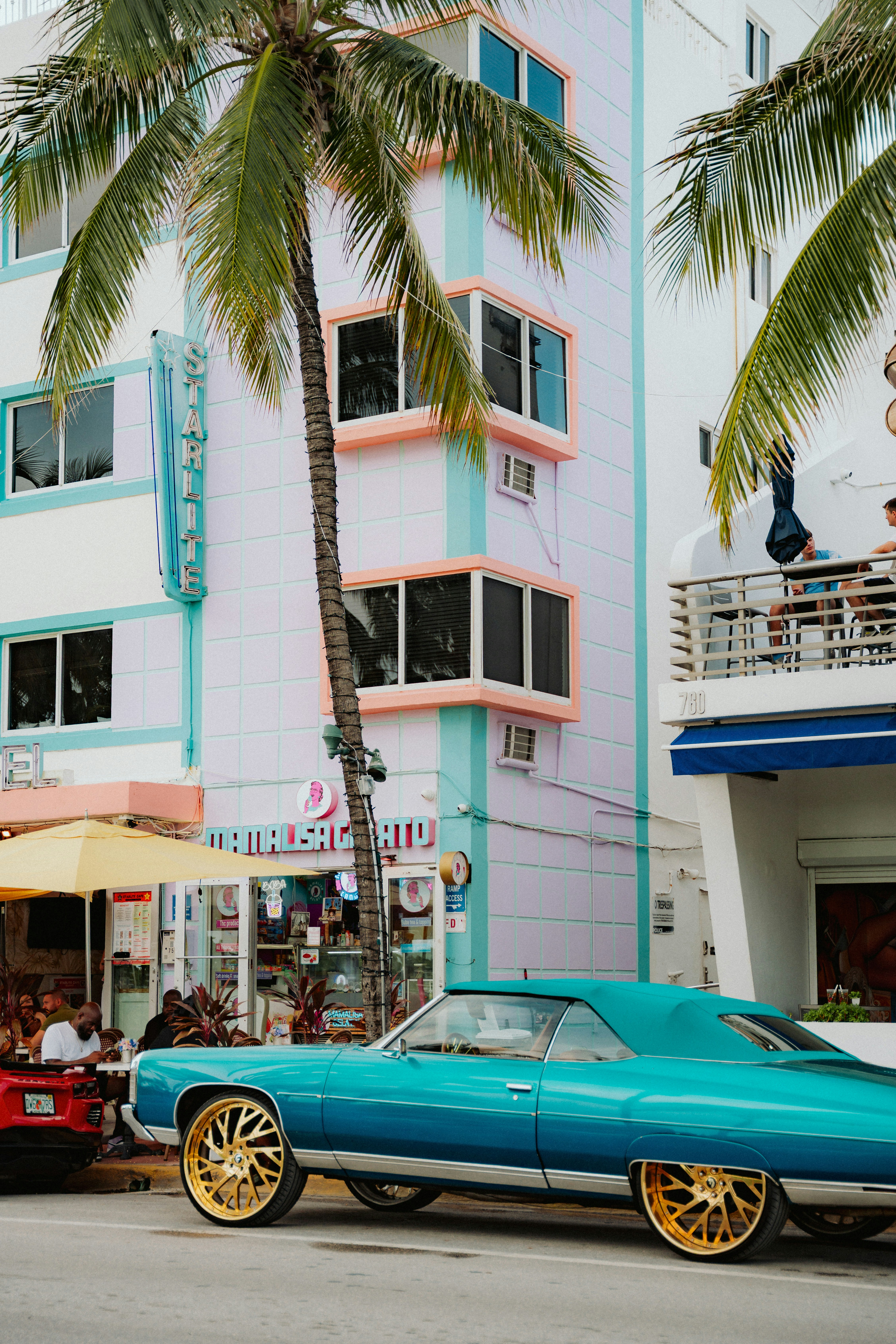 Turquoise classic car parked by pastel buildings and palm trees