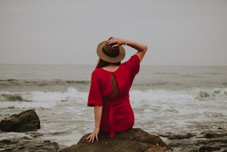Woman in red dress sits on rock by ocean