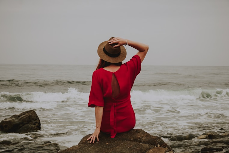 Woman in red dress sits on rock by ocean