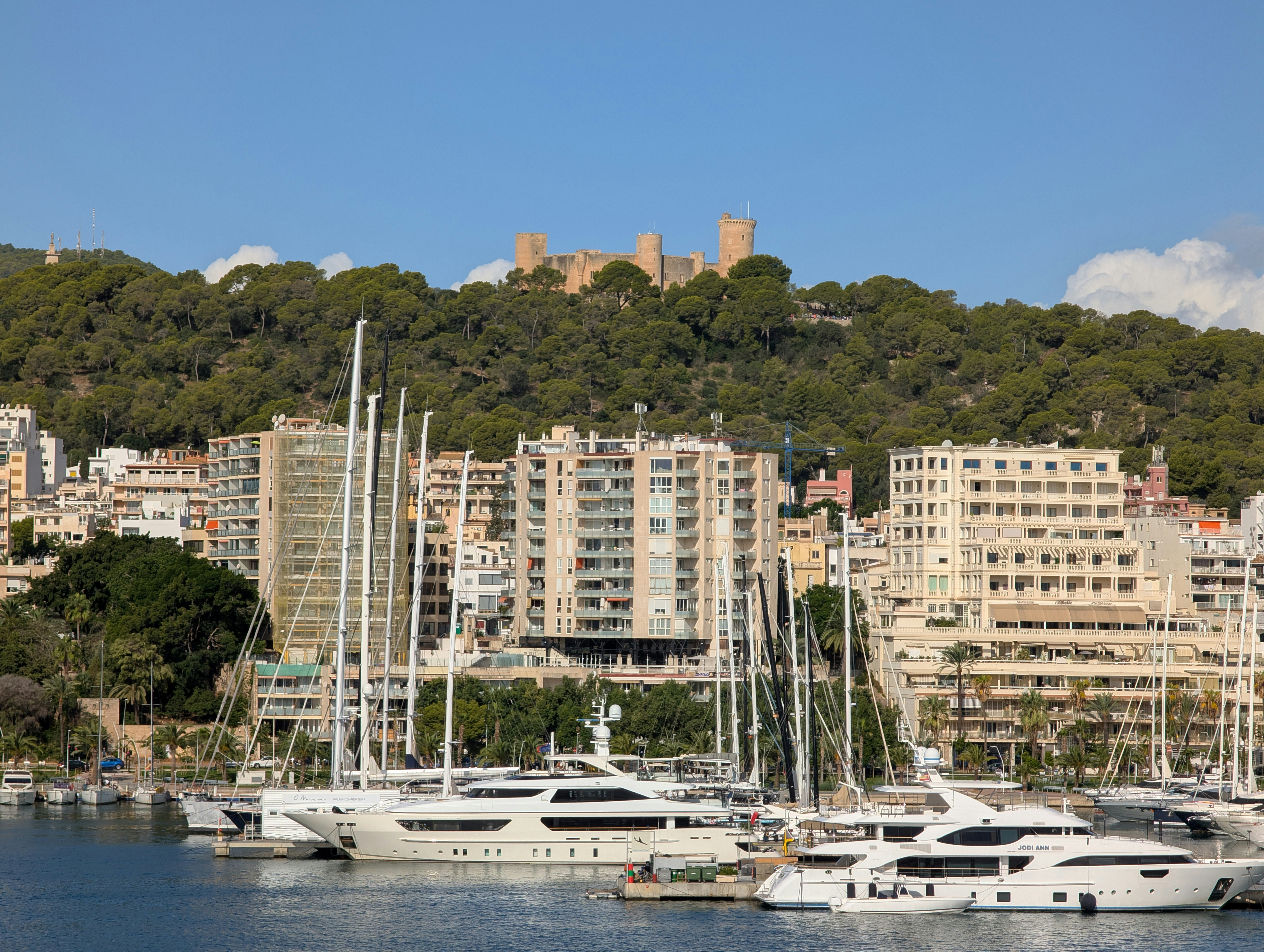 Luxury yachts docked in a harbor with cityscape and castle.