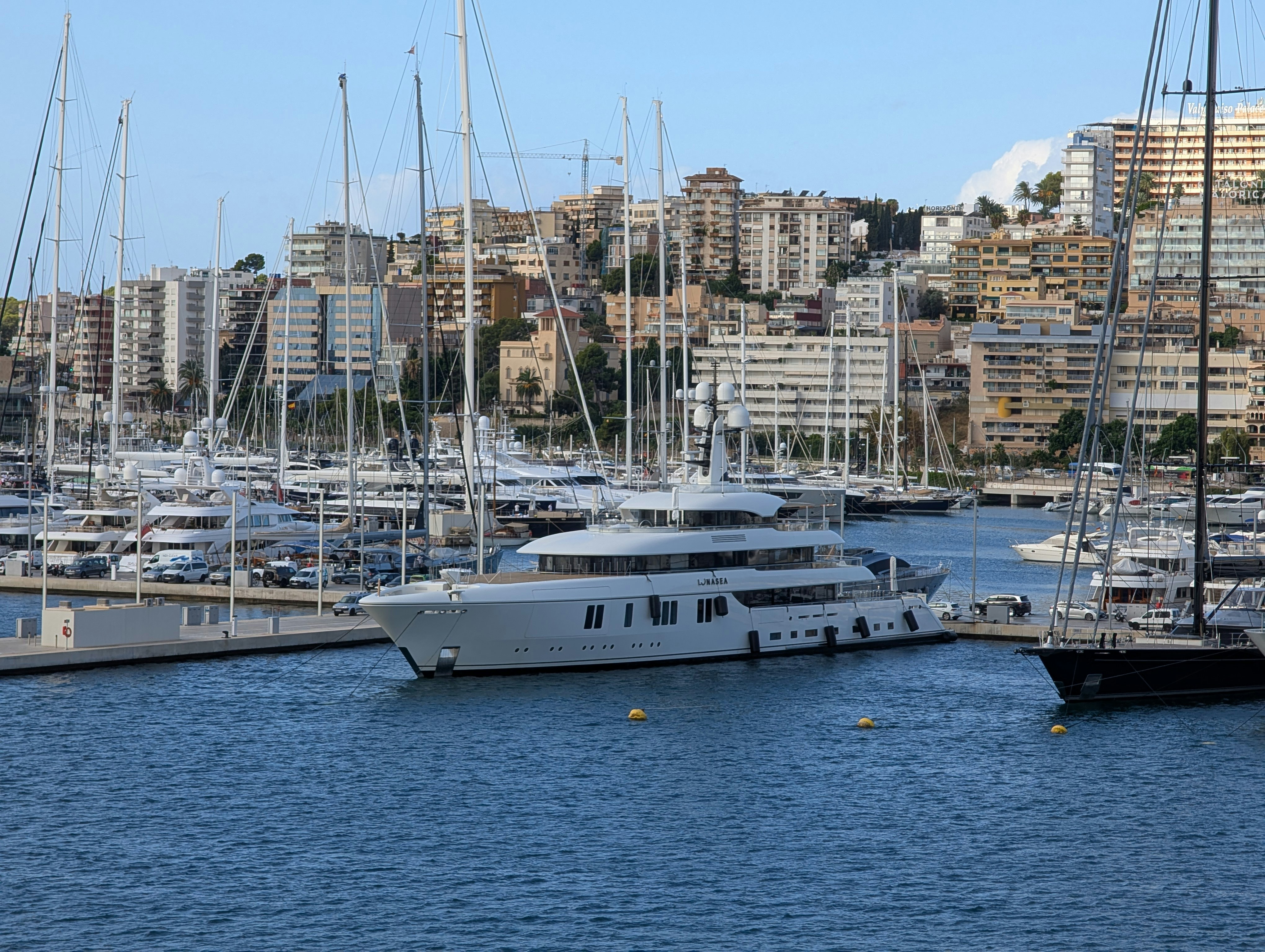 Large white yacht docked in a busy harbor.