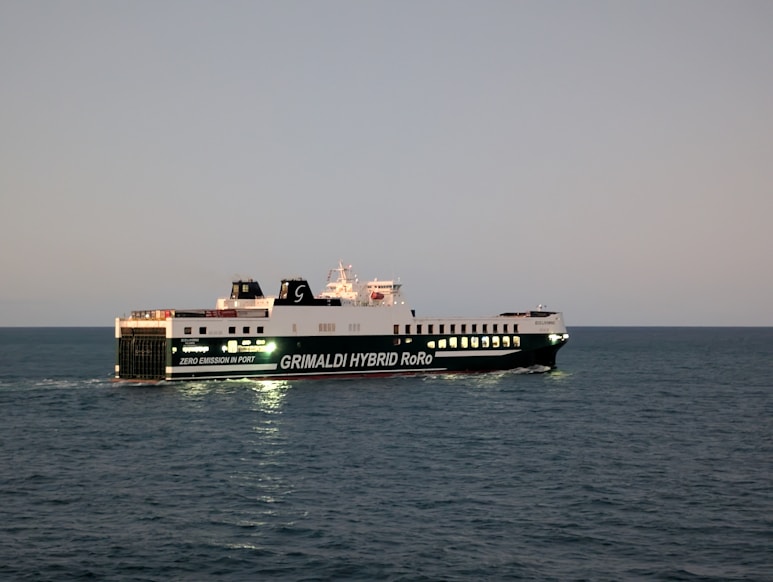 A large ferry sails on the ocean at dusk.