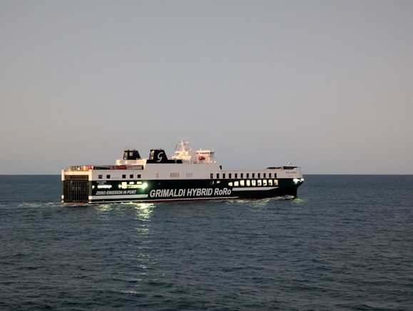 A large ferry sails on the ocean at dusk.