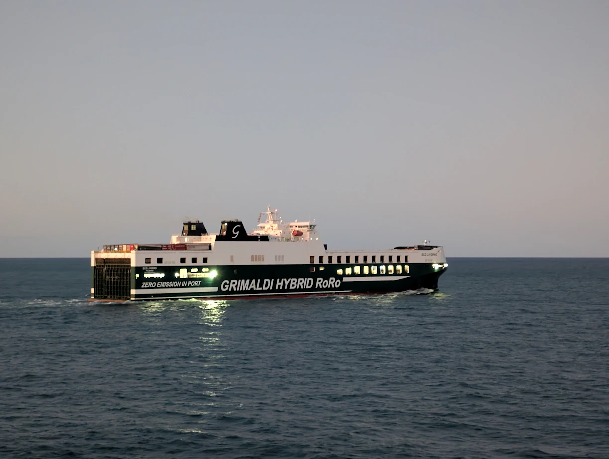A large ferry sails on the ocean at dusk.