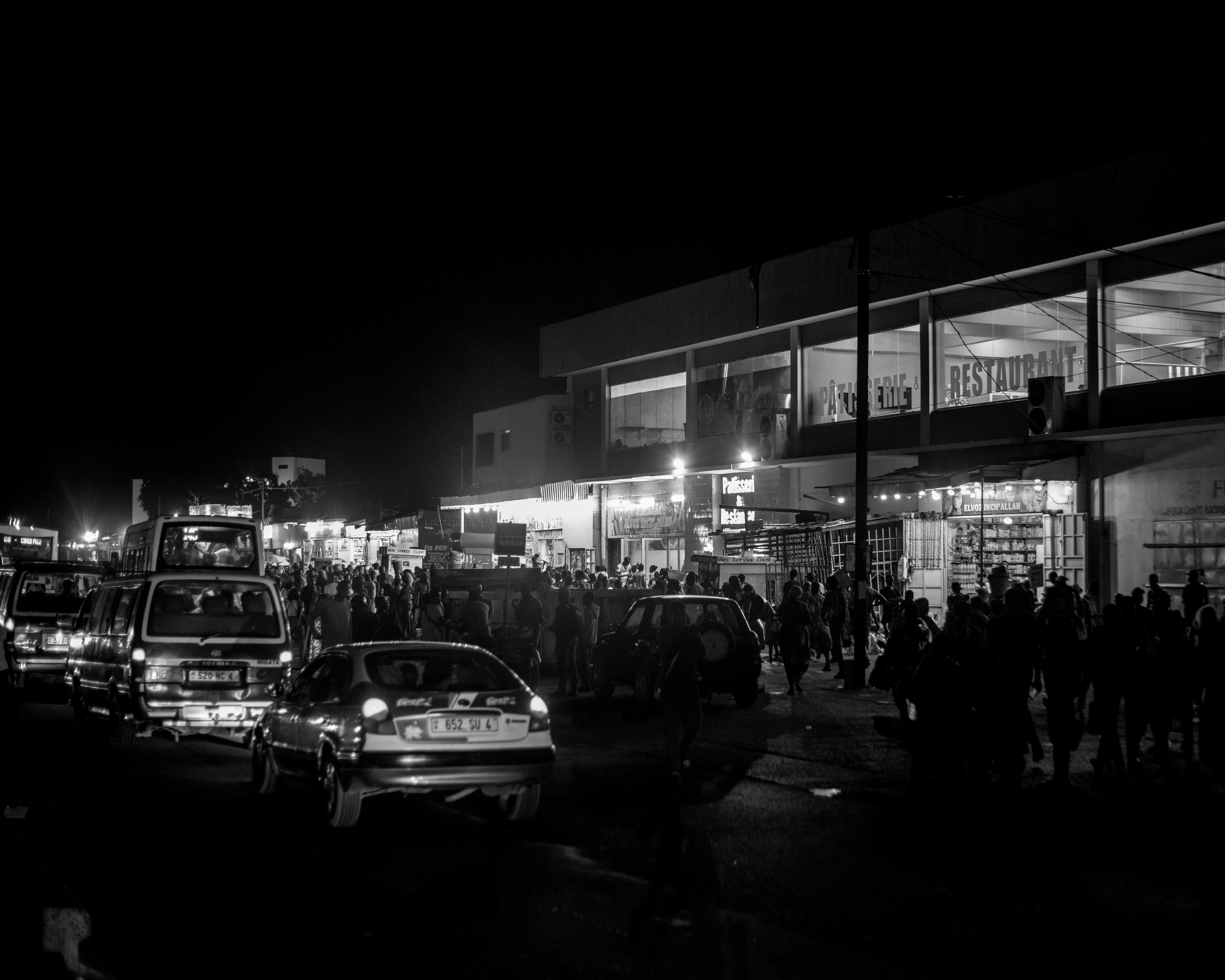 Cars and people outside a brightly lit building at night.