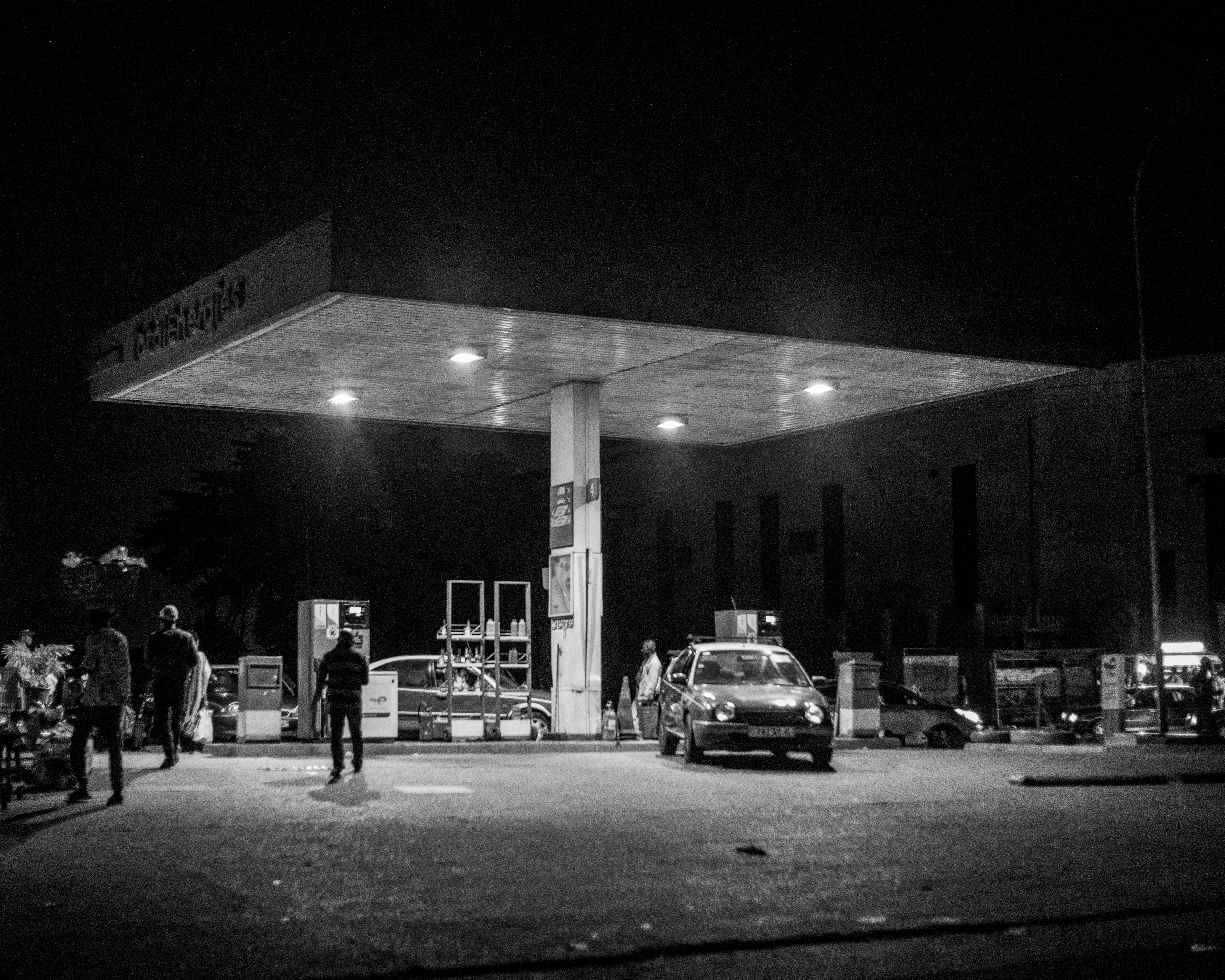 Pom bensin di malam hari dengan mobil dan orang-orang