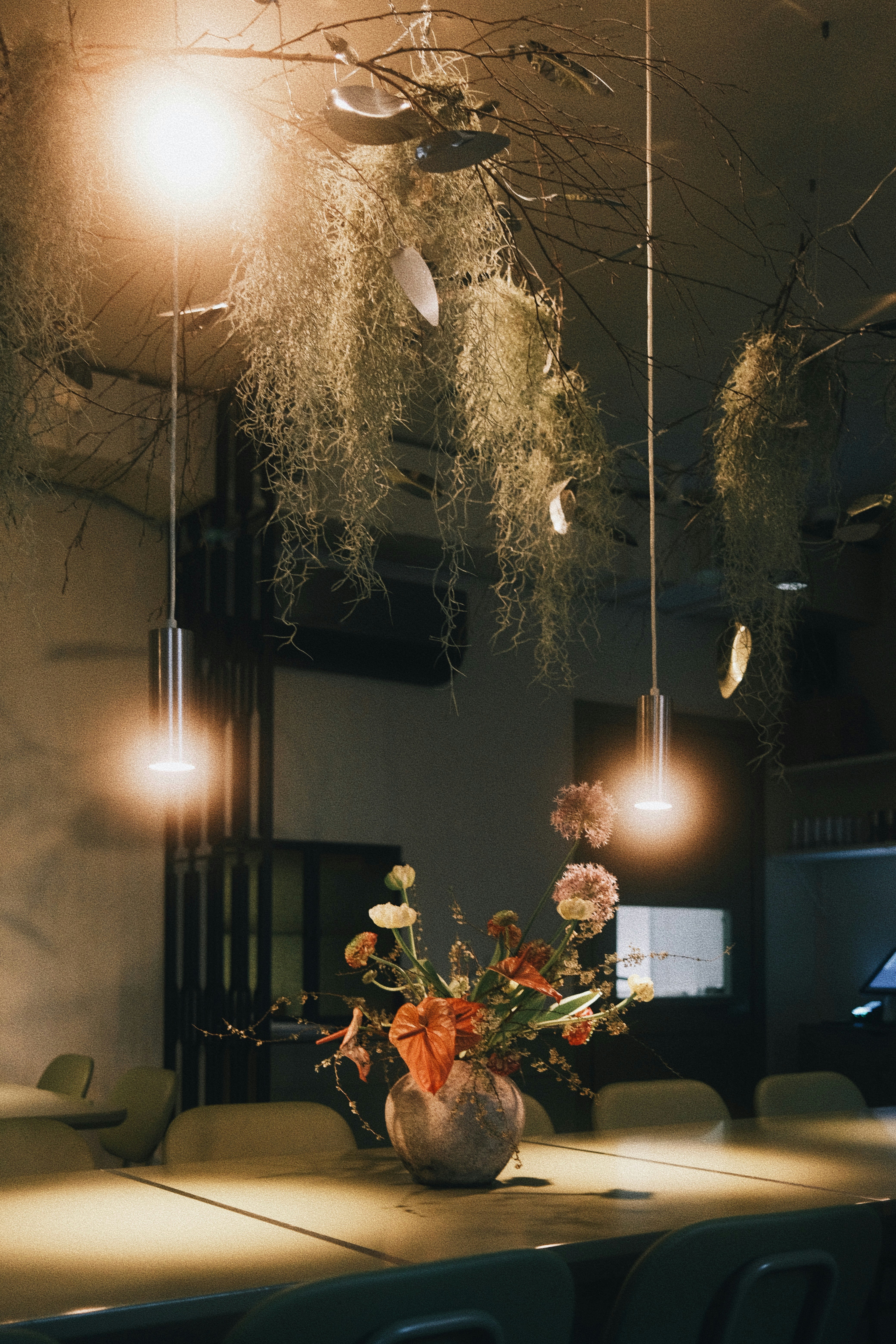 A floral arrangement sits on a table under hanging plants.