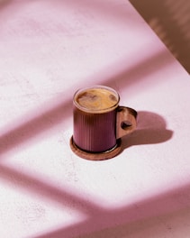 Glass mug with coffee on wooden coaster.