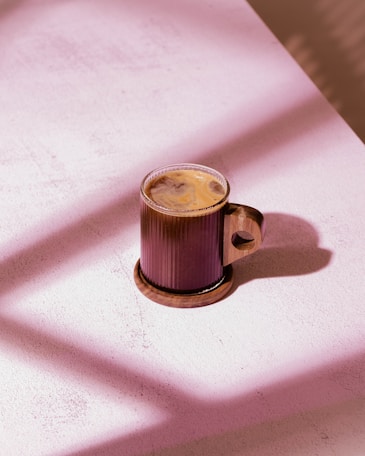 Glass mug with coffee on wooden coaster.