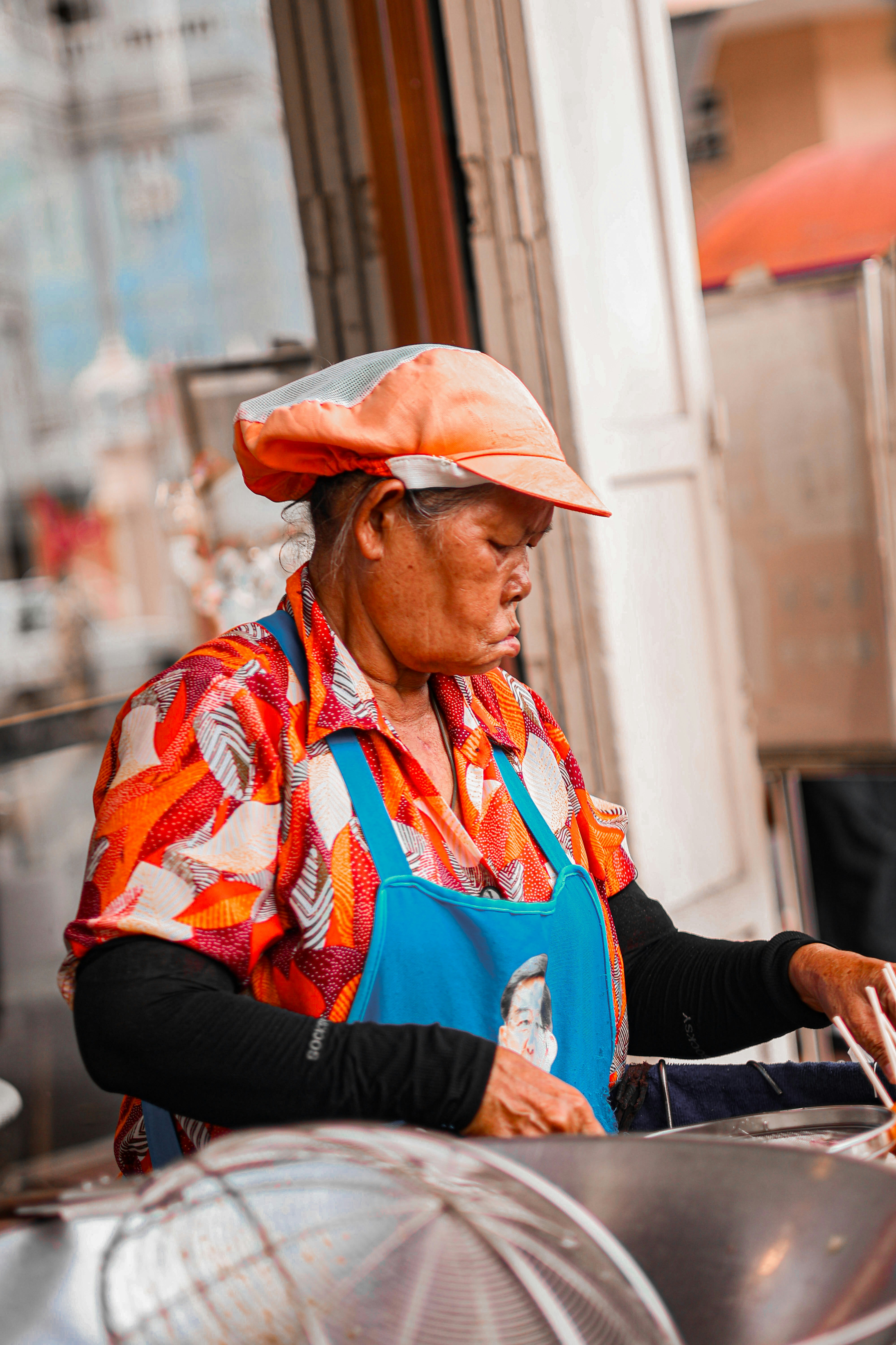 Elderly woman cooking food at an outdoor stall.