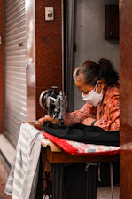 Mujer mayor con mascarilla cosiendo en una máquina antigua.