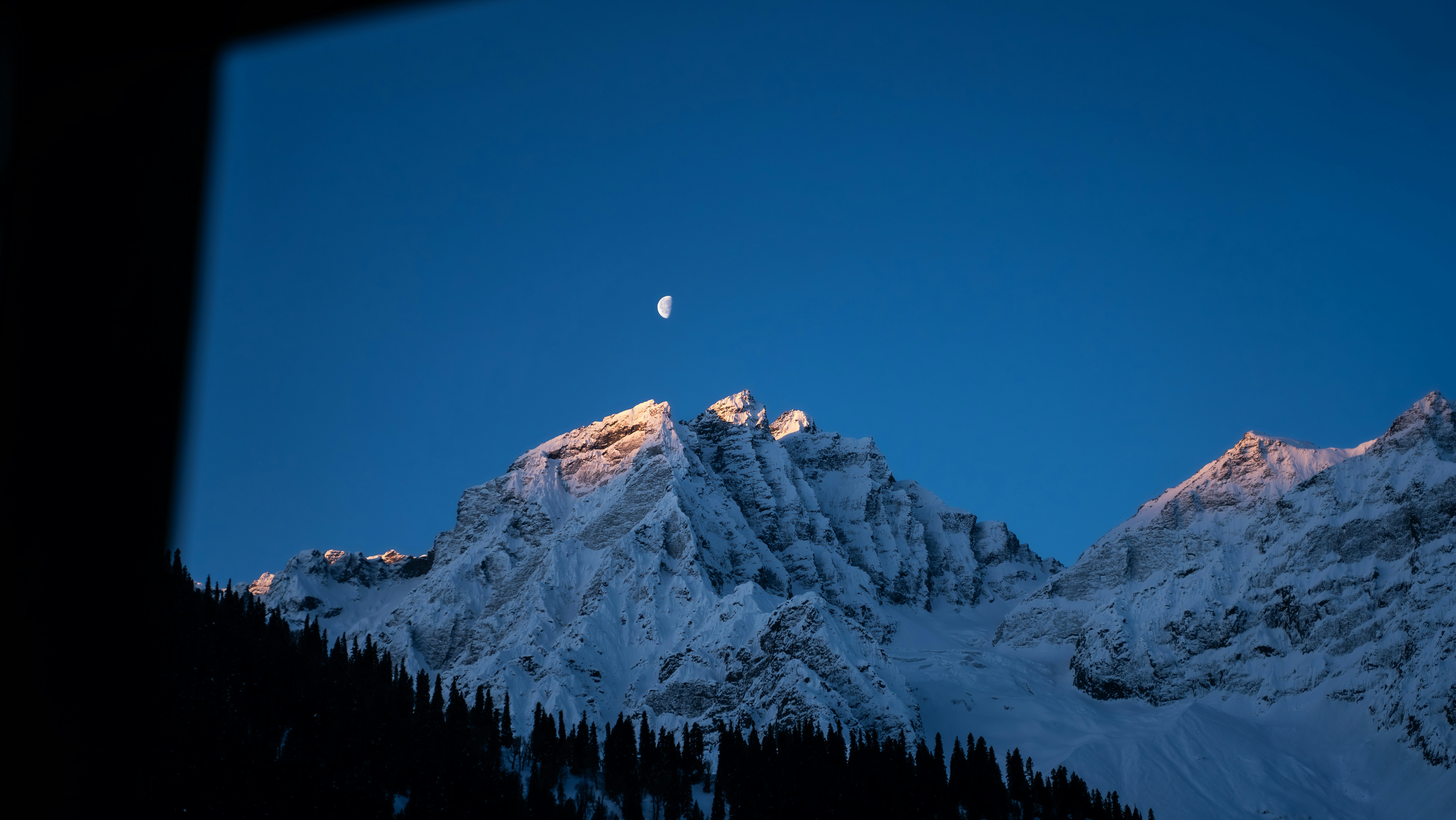 Moonlit snow-capped mountains under a clear blue sky.
