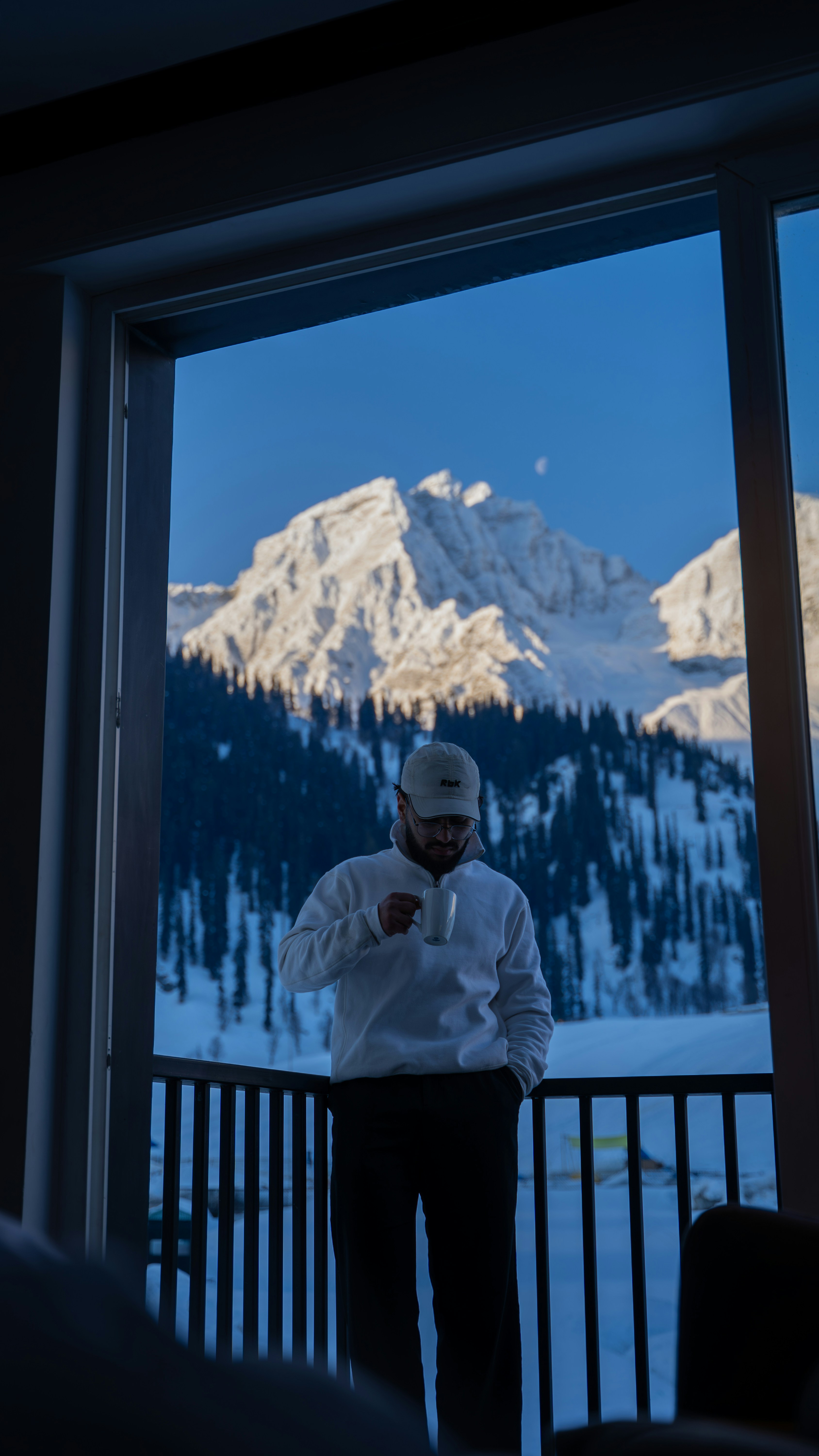 Man holding coffee cup on balcony with snowy mountains