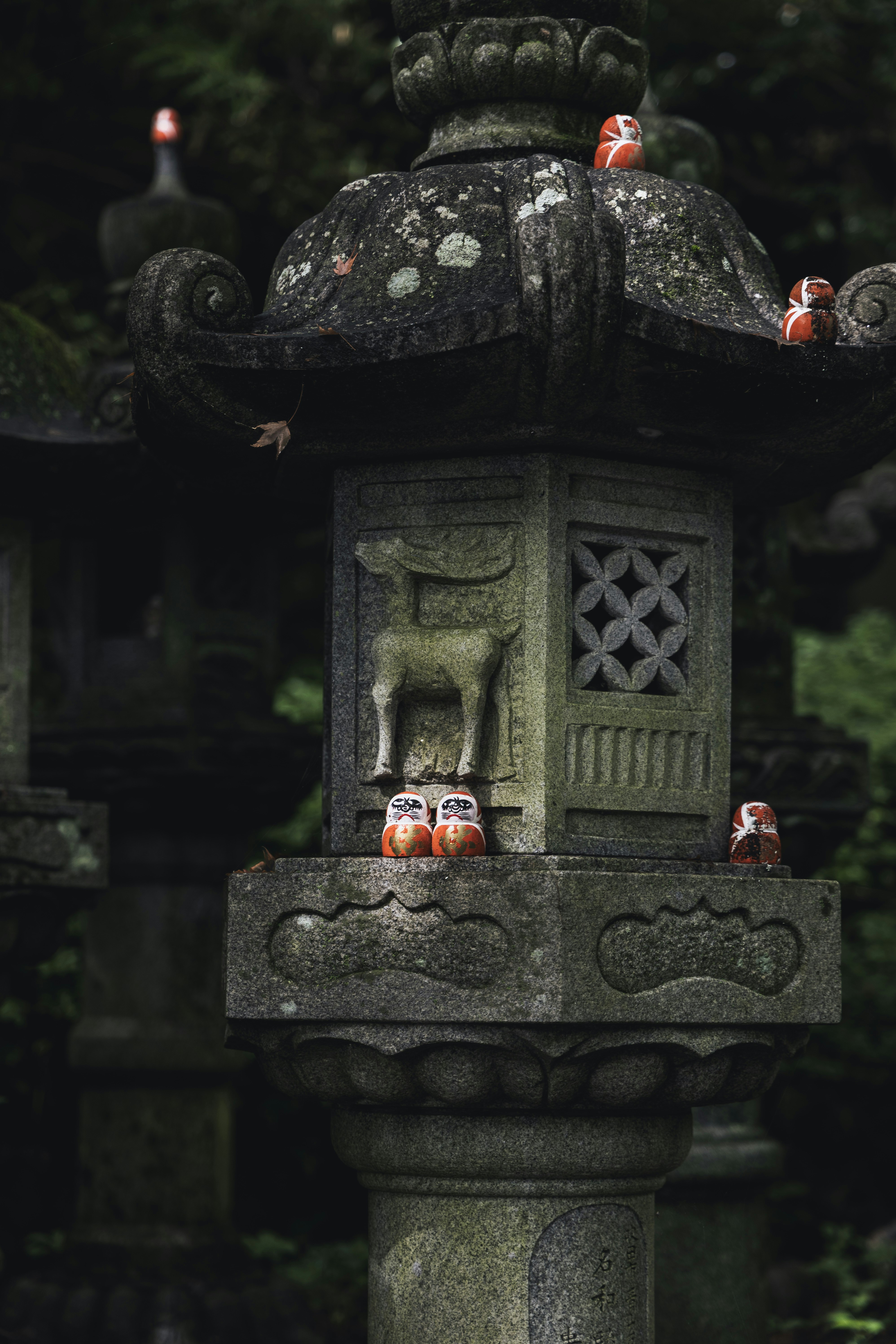 Stone lantern decorated with small daruma dolls.