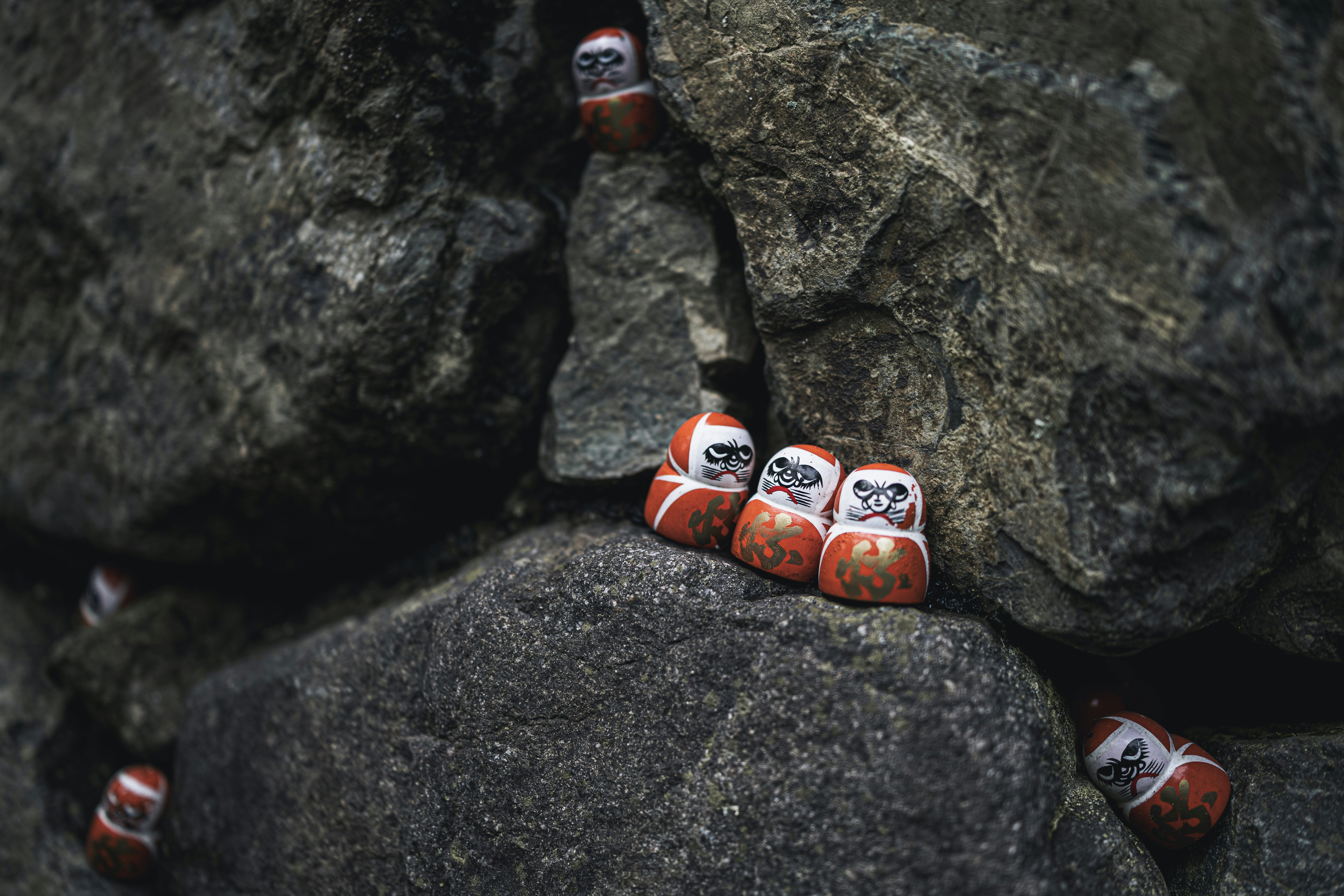 Several daruma dolls rest on rocky surfaces.