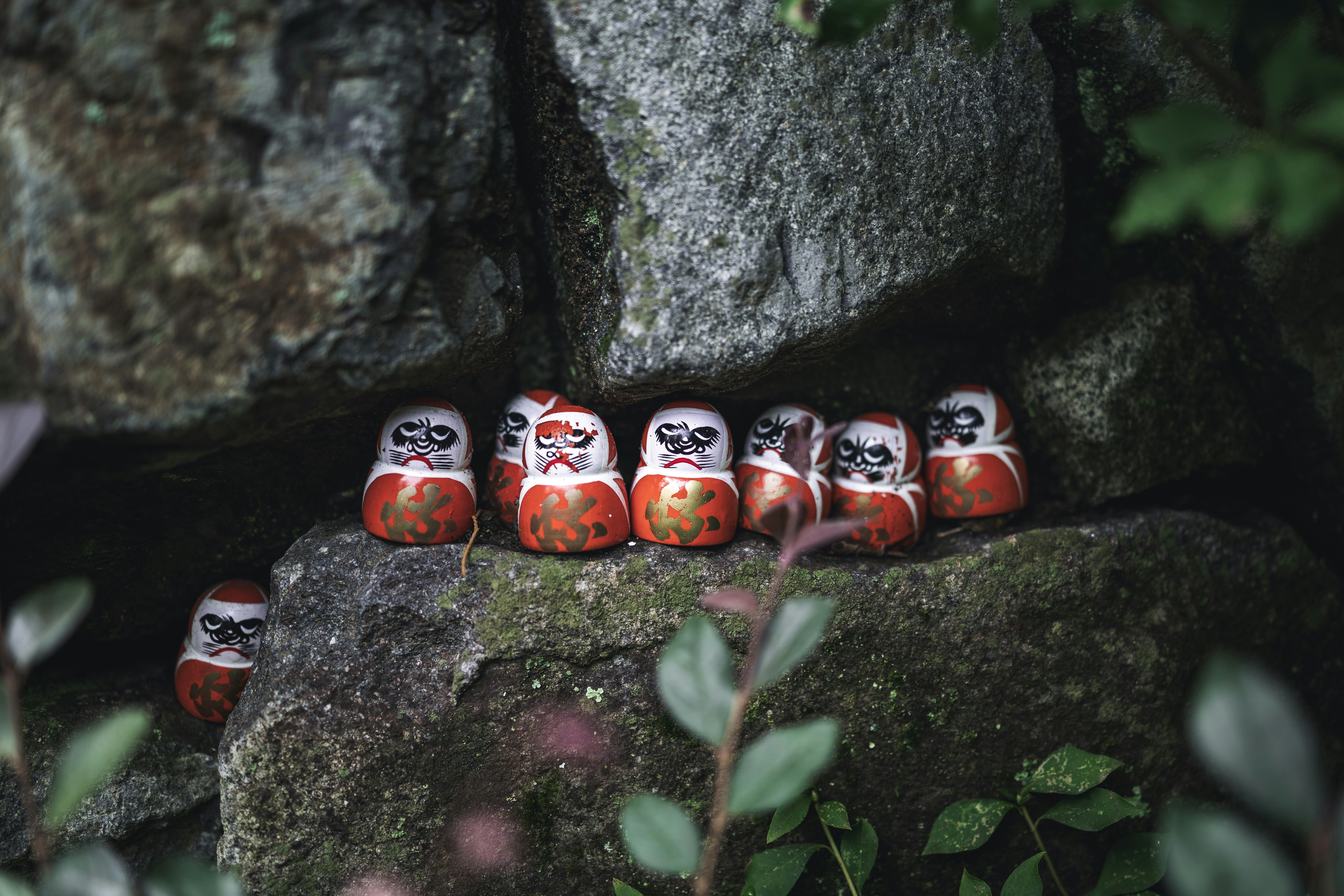 Several small daruma dolls nestled among rocks.