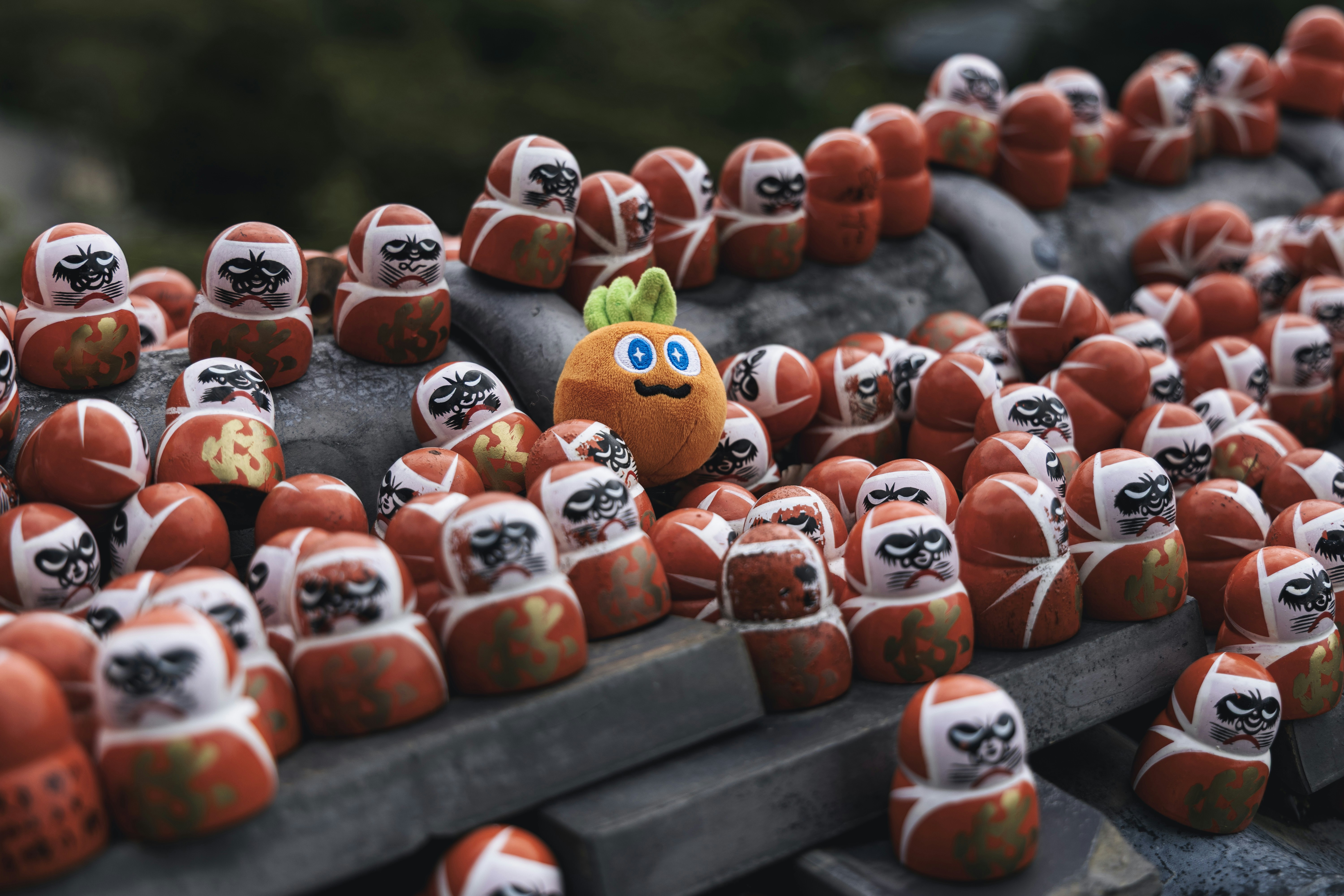 Many daruma dolls with one orange character doll.