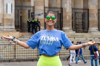 Woman in blue zumba shirt and green sunglasses smiles.
