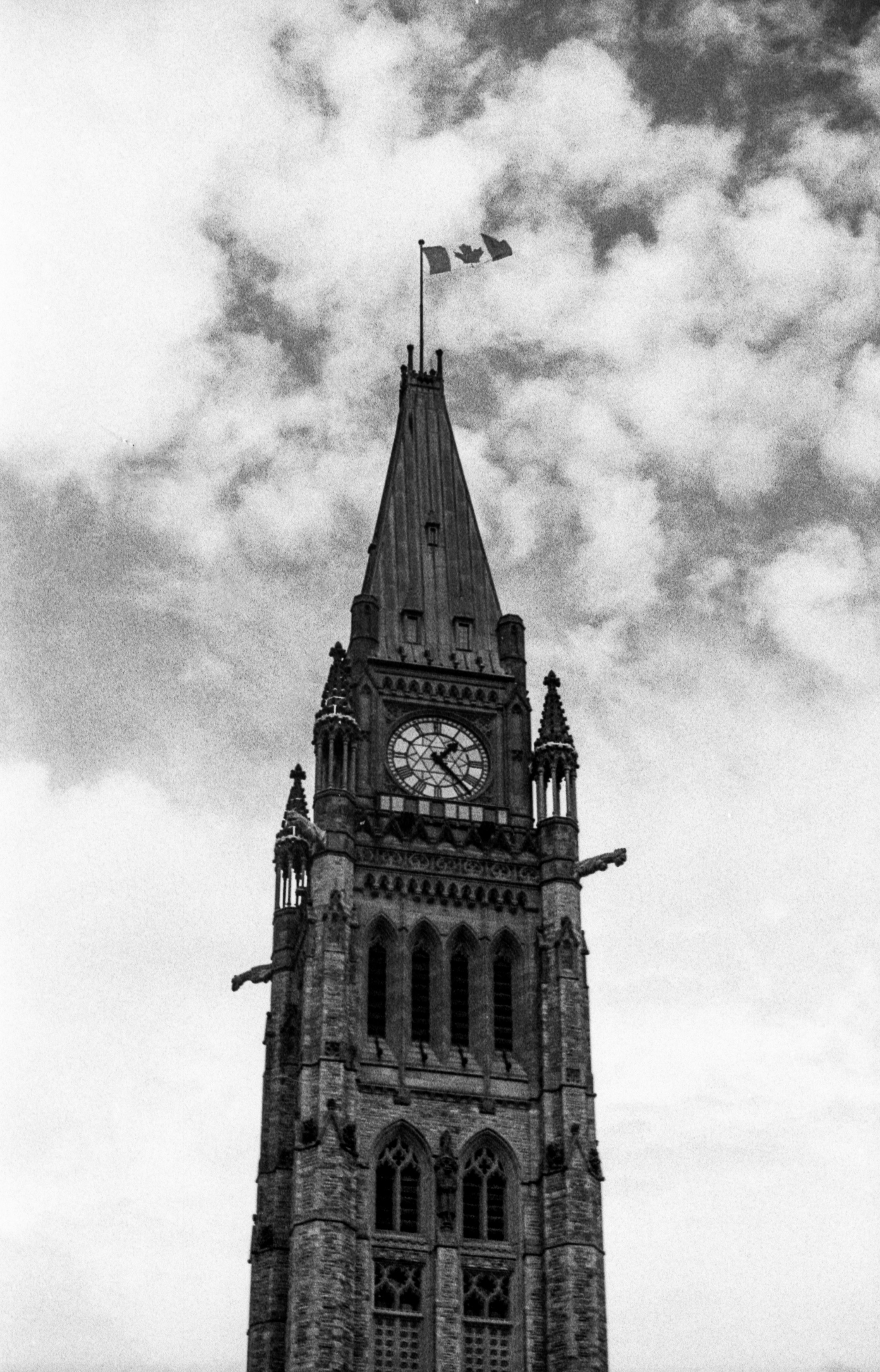 Clock tower with canadian flags against cloudy sky
