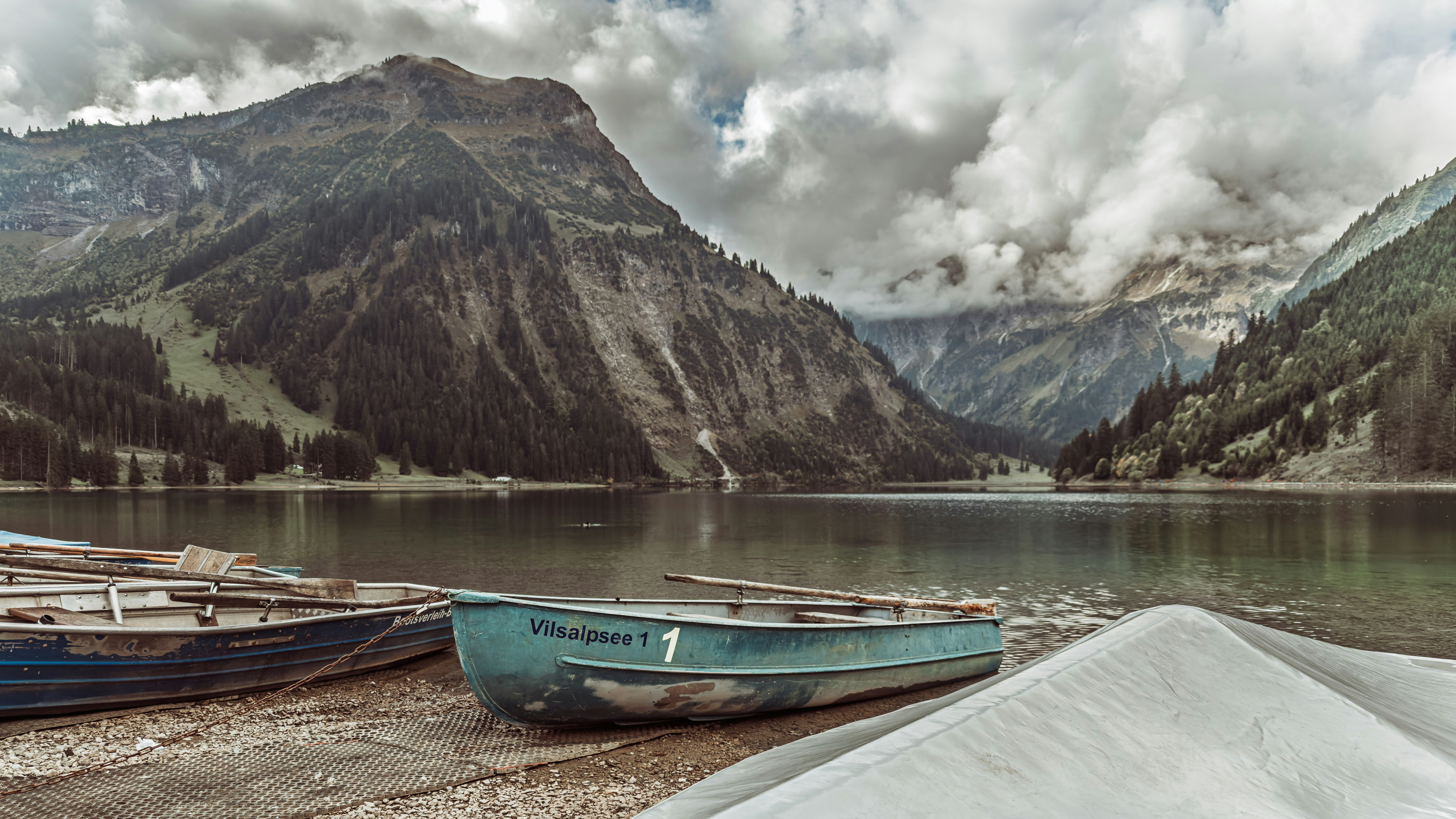 Boats rest on a shore with a mountain lake backdrop.
