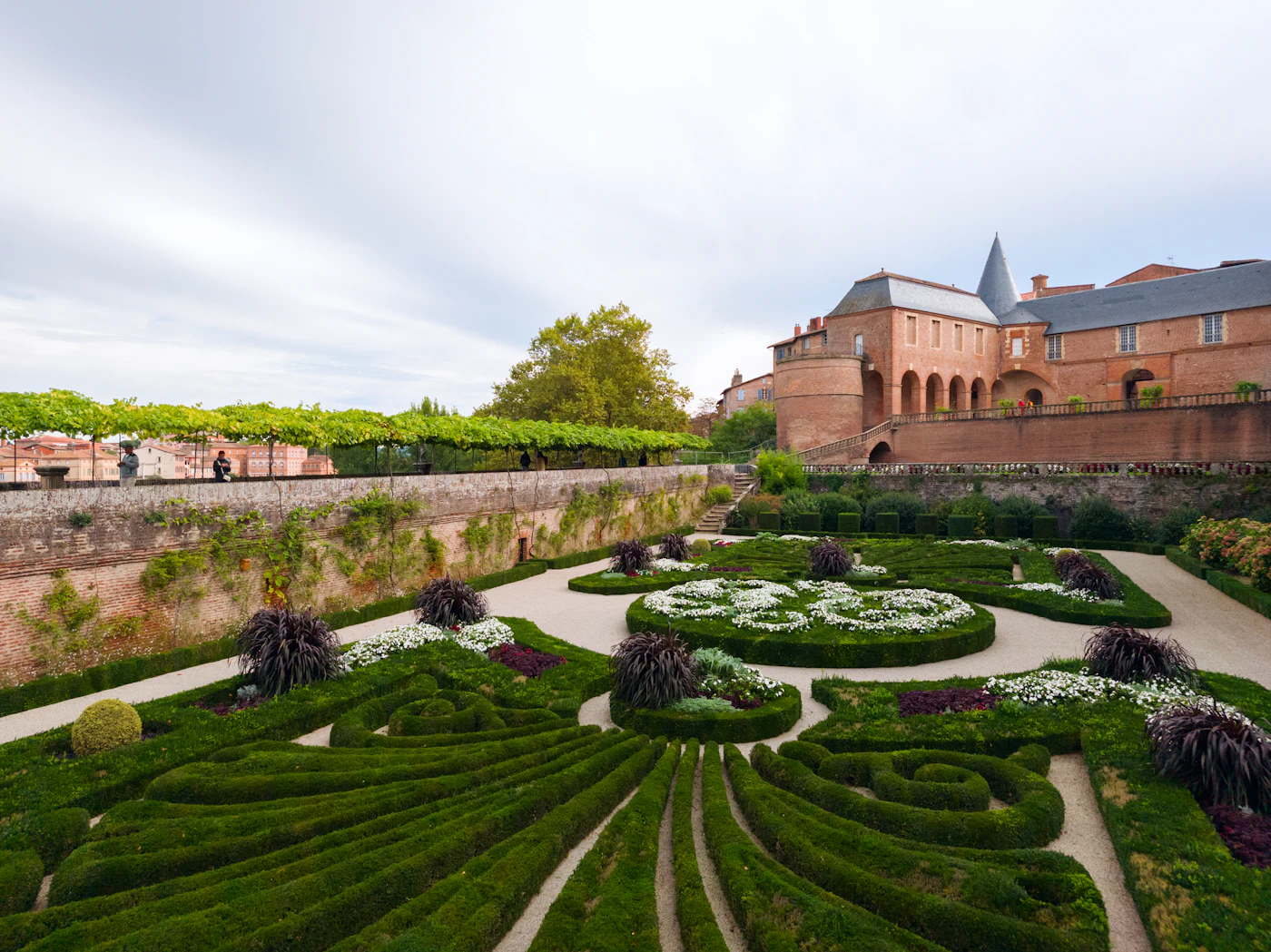 A formal garden with manicured hedges leading to a brick building.