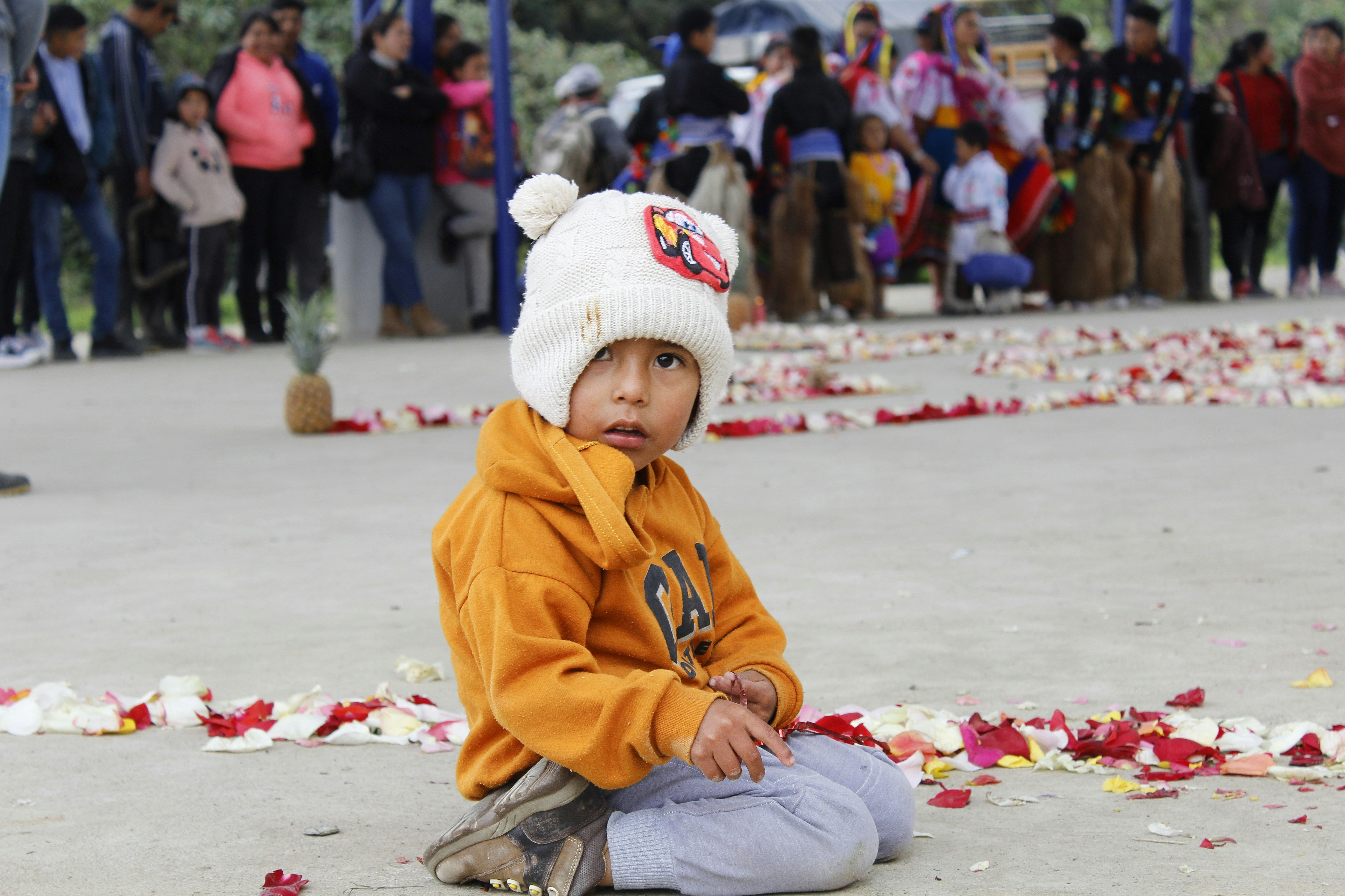 Young child in orange hoodie sits on ground with flowers