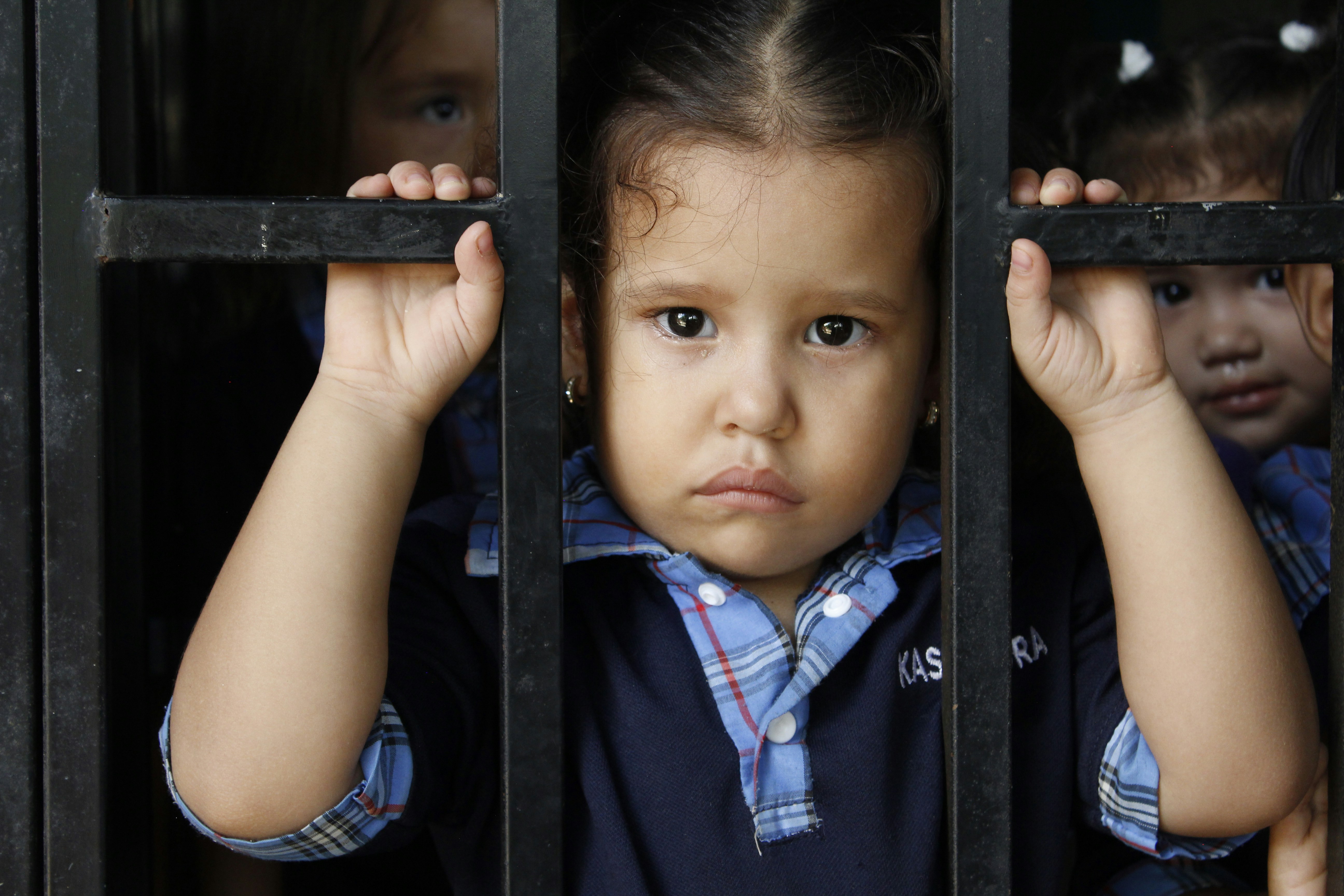 Three young children behind a metal grate