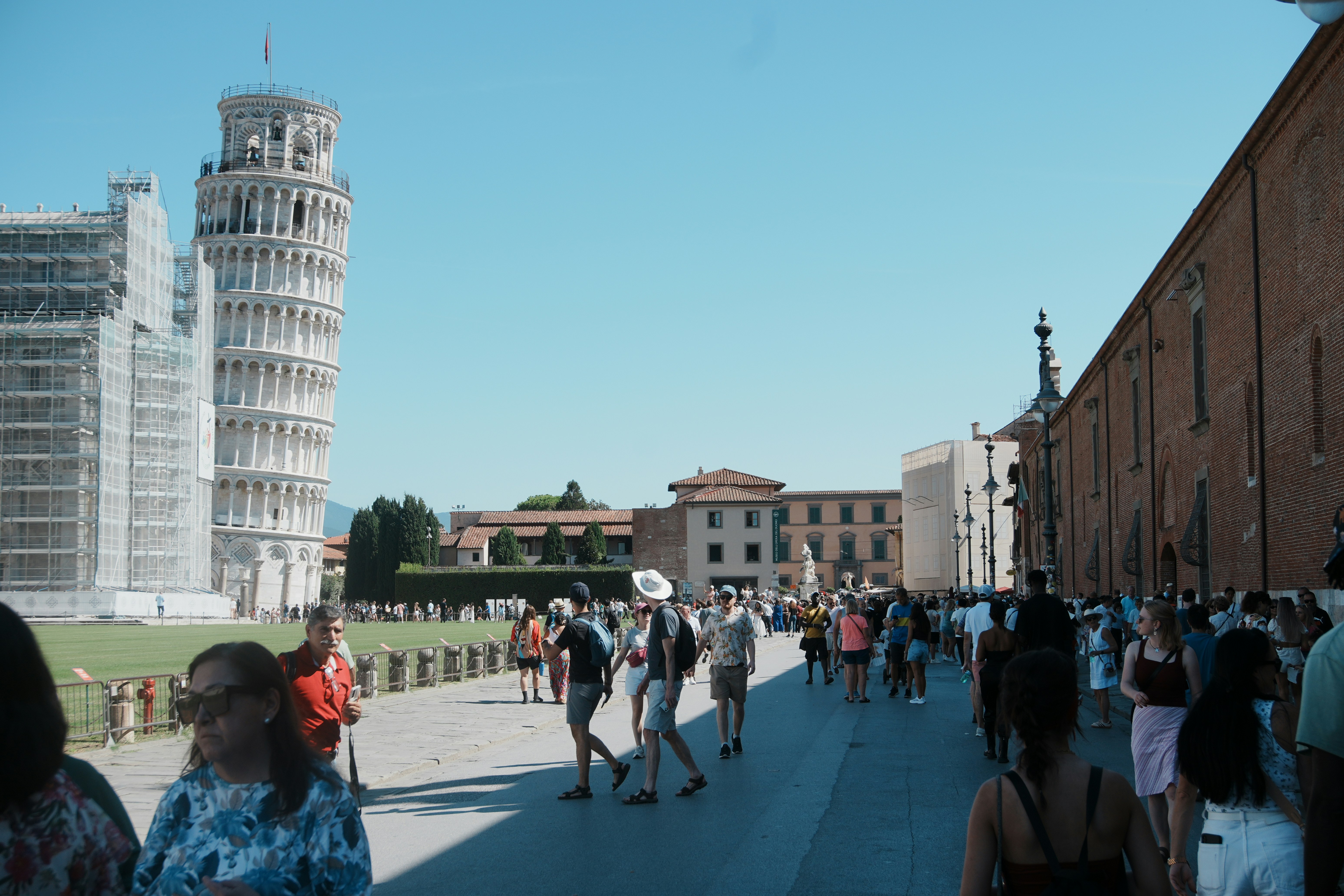 Tourists walk towards the leaning tower of pisa.