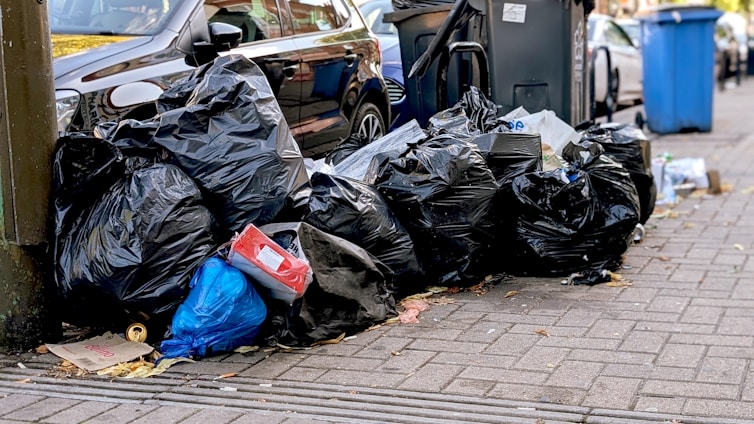 Pile of black trash bags on a sidewalk.