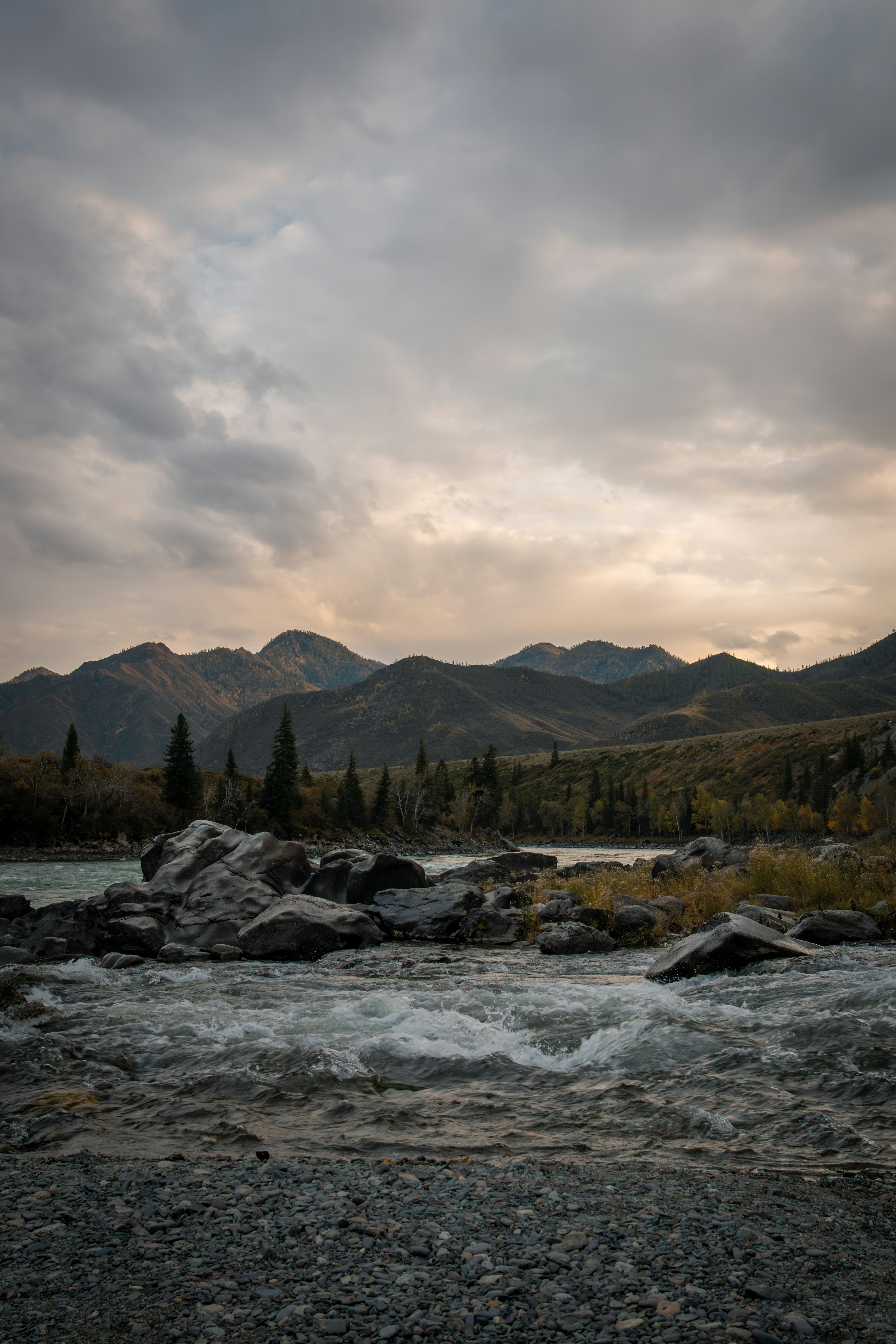 Mountain range with river and forest under cloudy sky