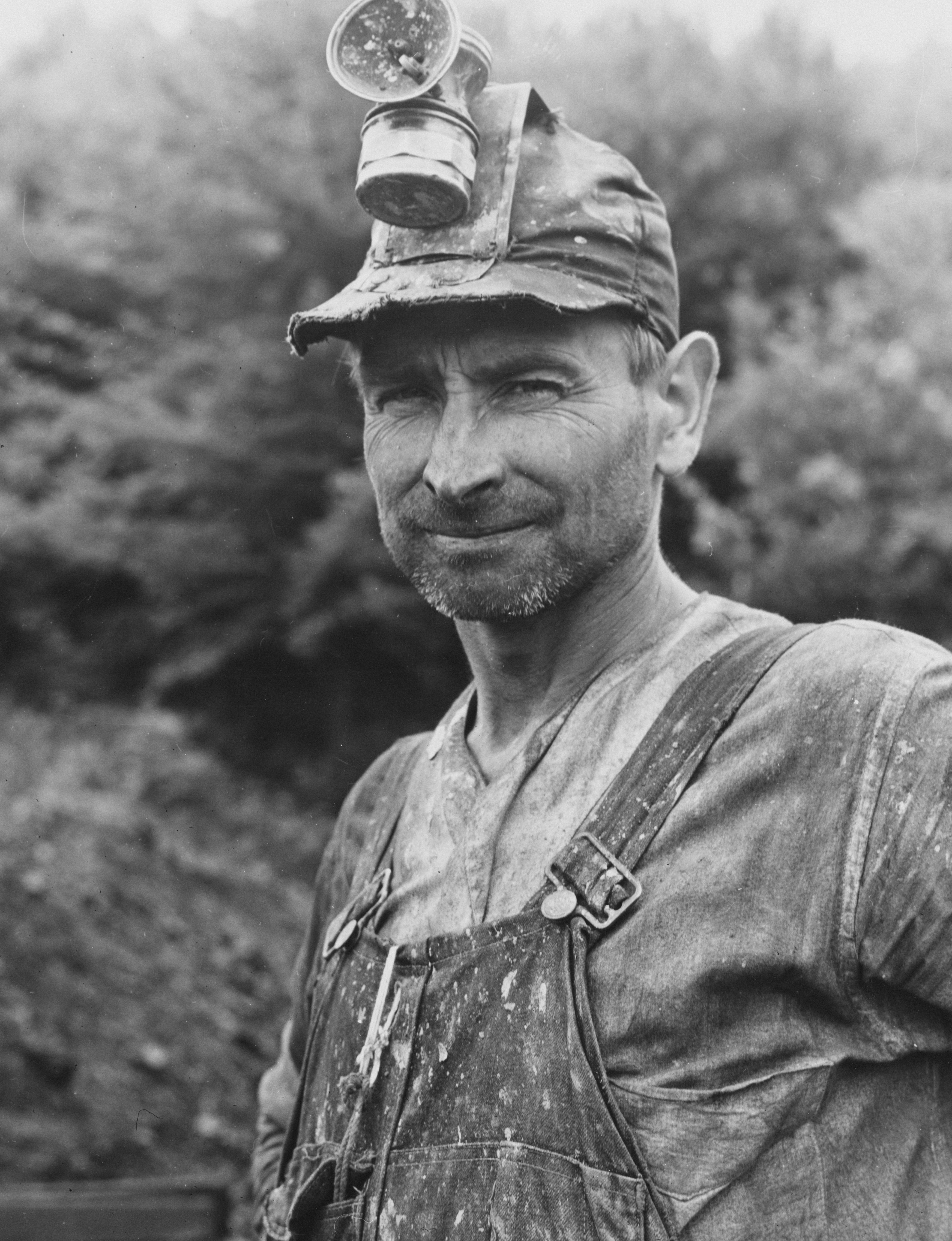 A miner wearing a headlamp and dirty overalls.