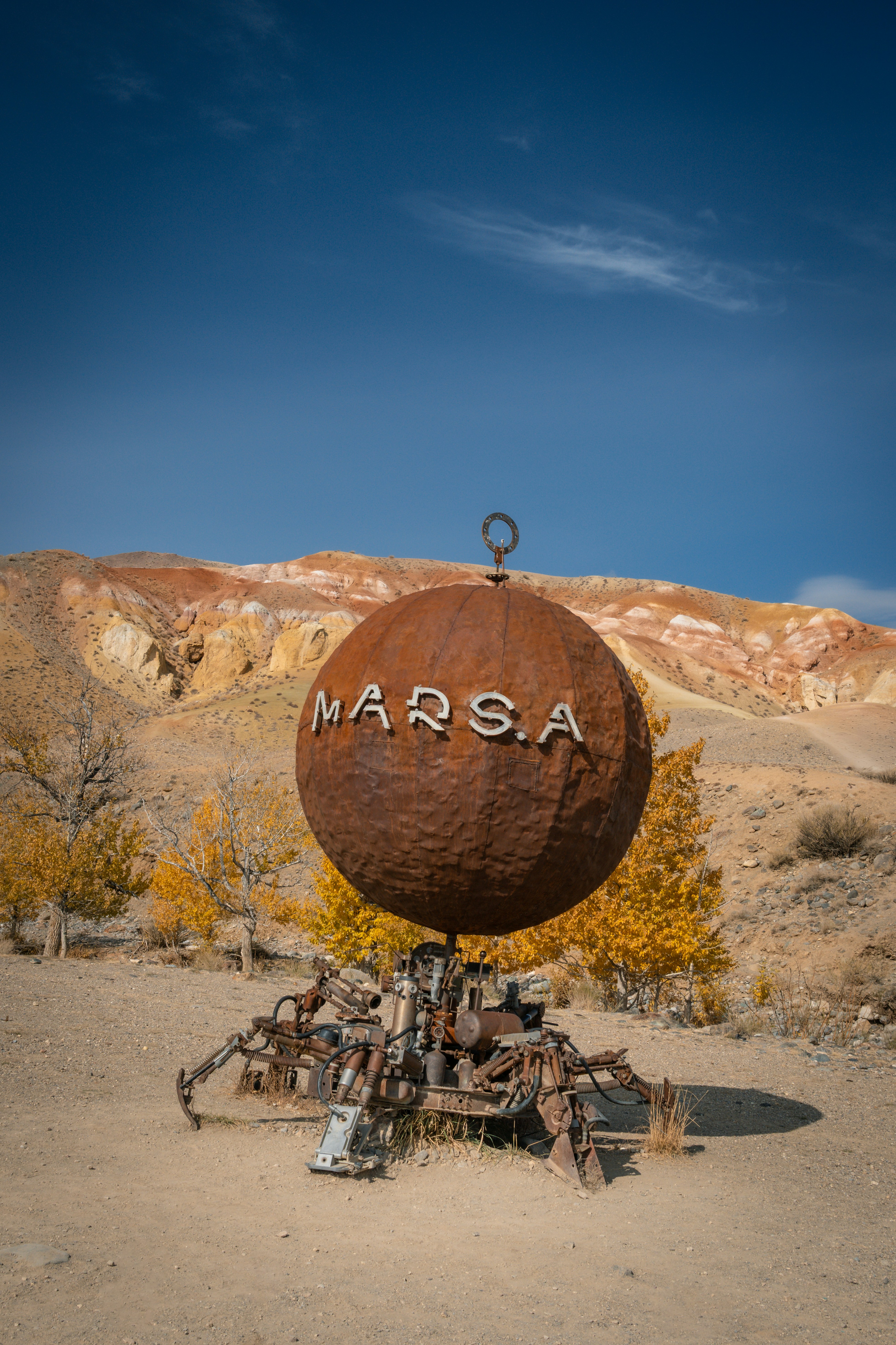 Rusty sphere sculpture with mars.a text in desert landscape.