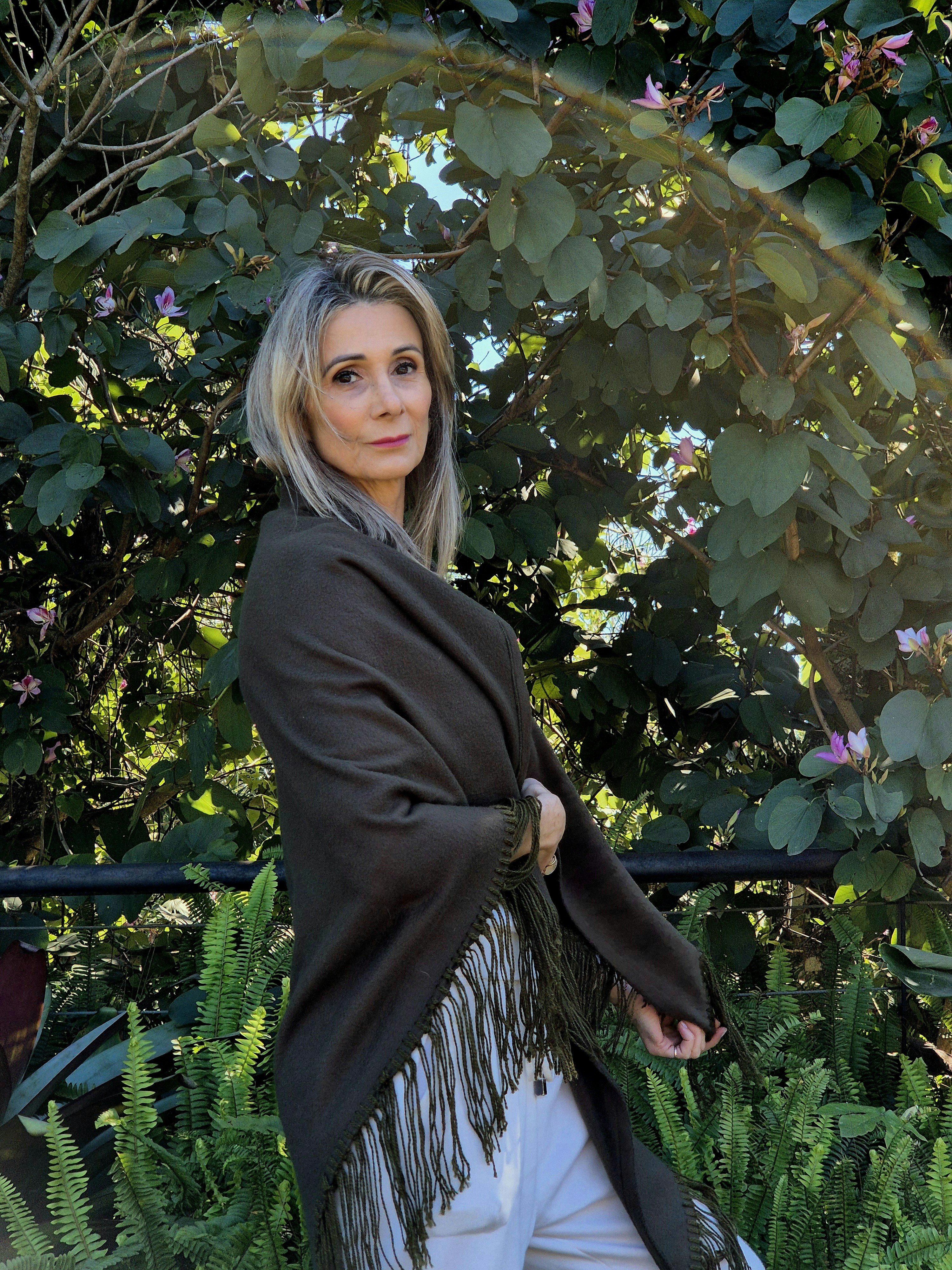 屋外の植物の近くに立っているショールを着た女性。