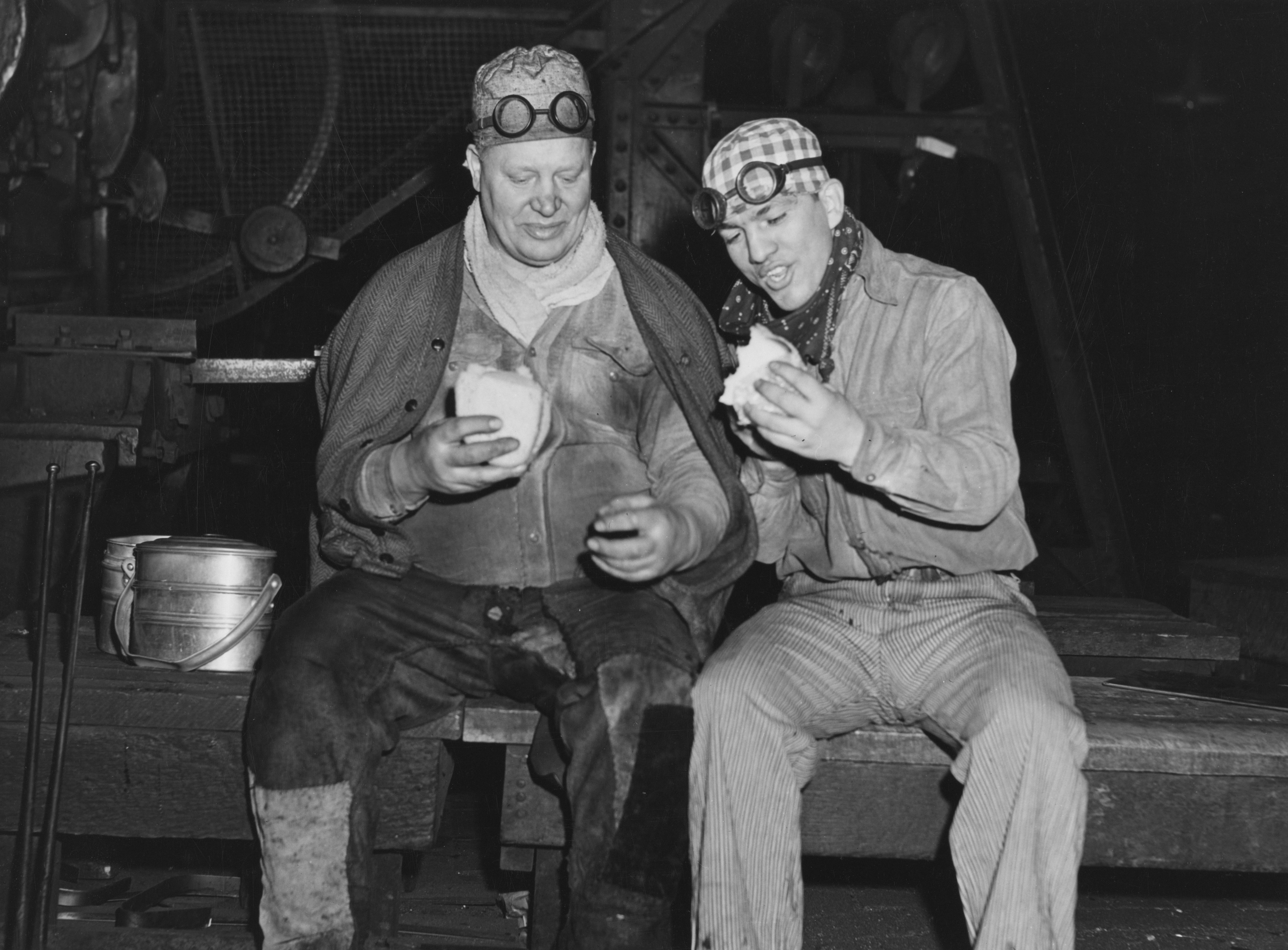 Two men in work clothes eating sandwiches